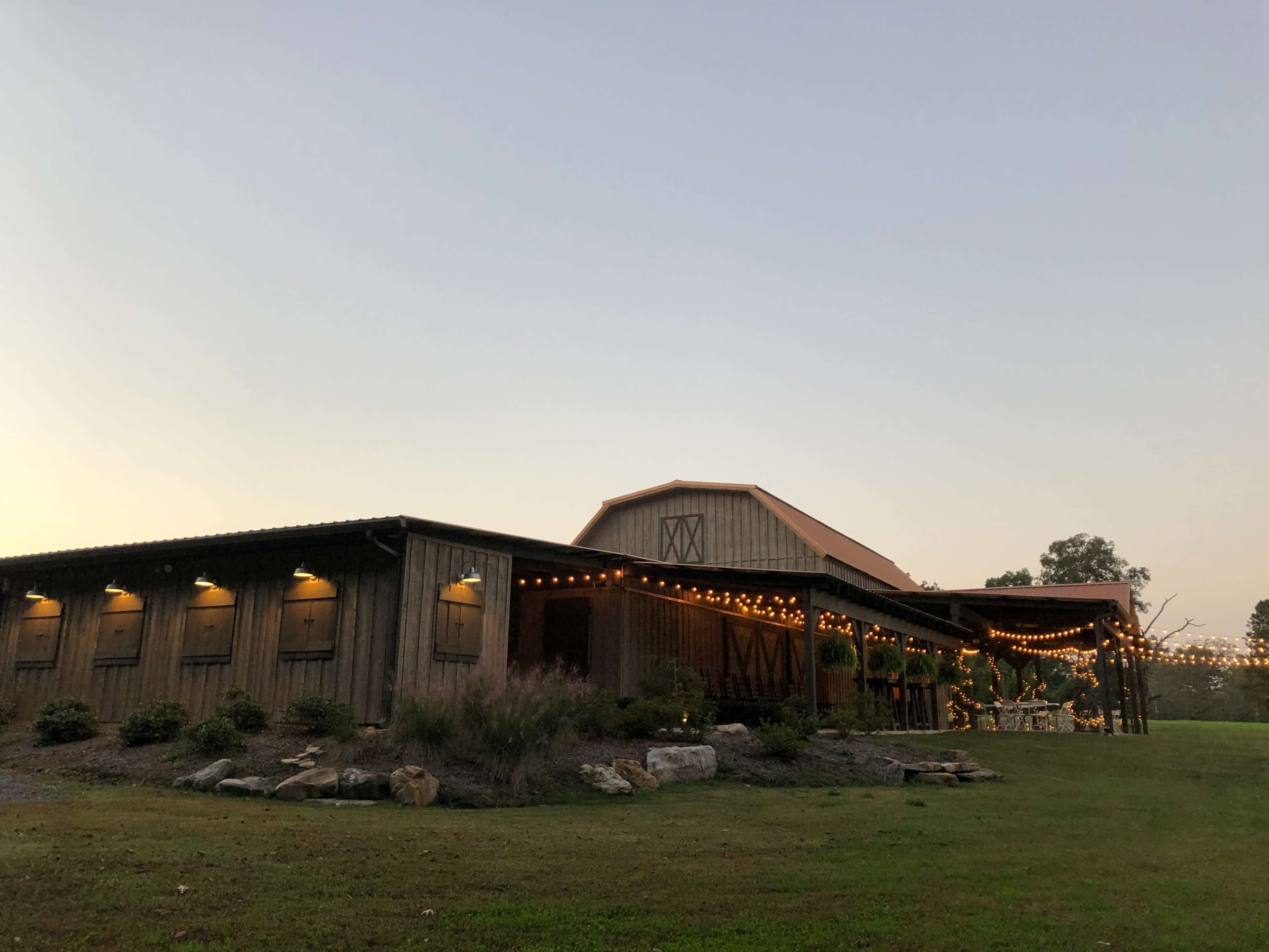 A wooden barn-style building decorated with string lights, set against a twilight sky.