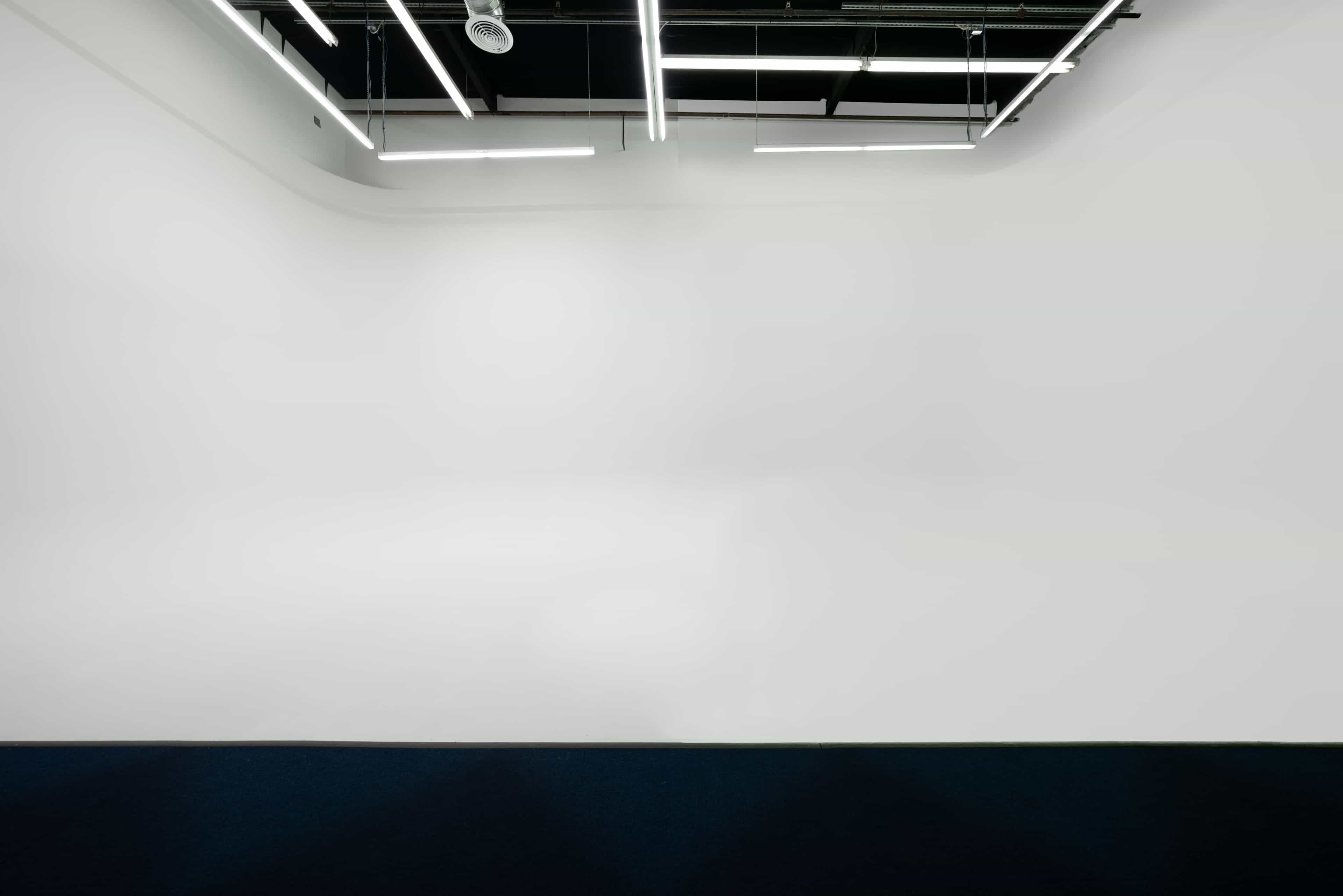 A minimalistic interior space with white walls and ceiling, illuminated by linear lighting fixtures.