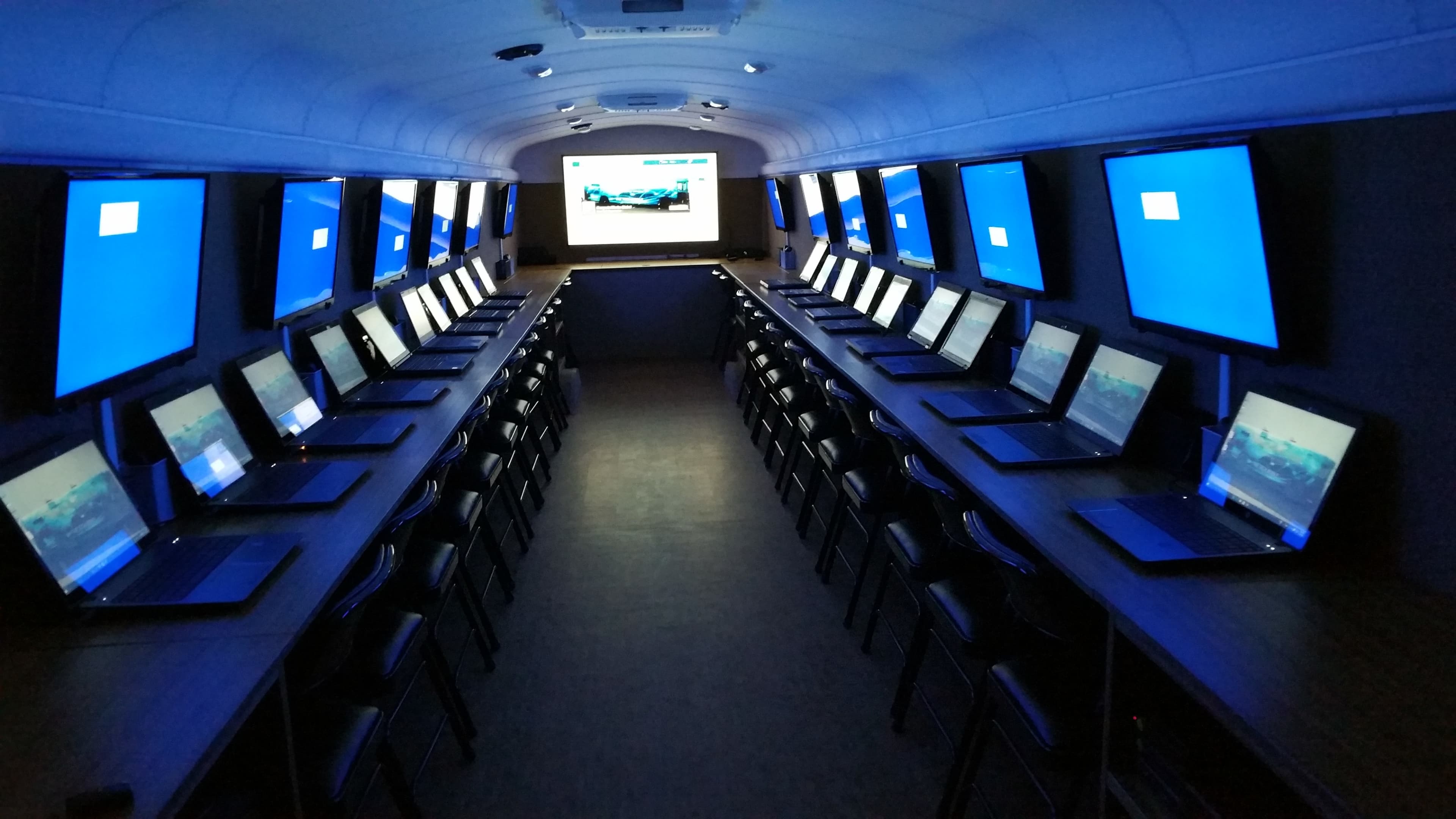A row of tables in a dark room is lined with laptops and large screens displaying blue screens.
