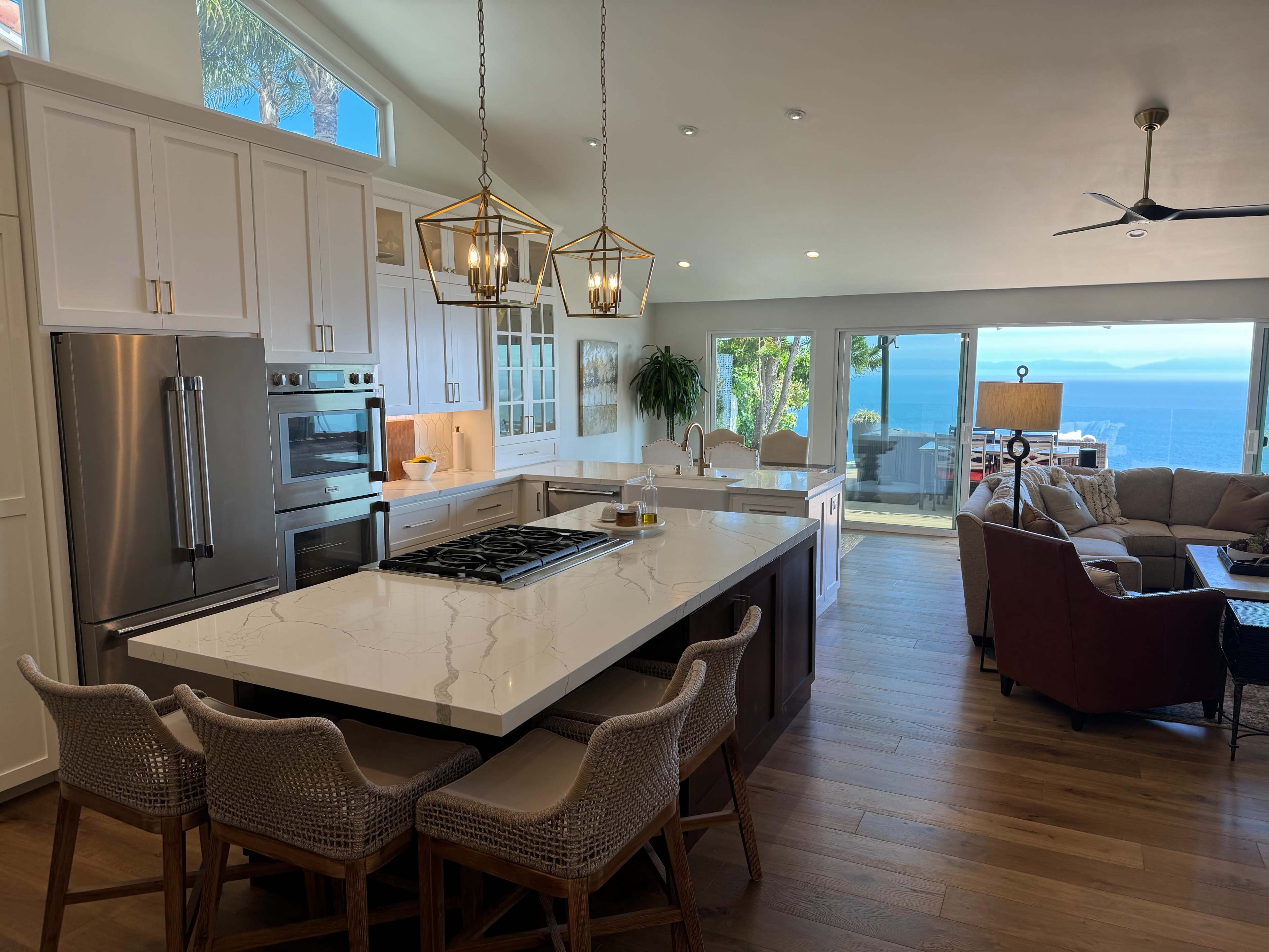 A modern kitchen with a large island and a panoramic ocean view through glass doors.