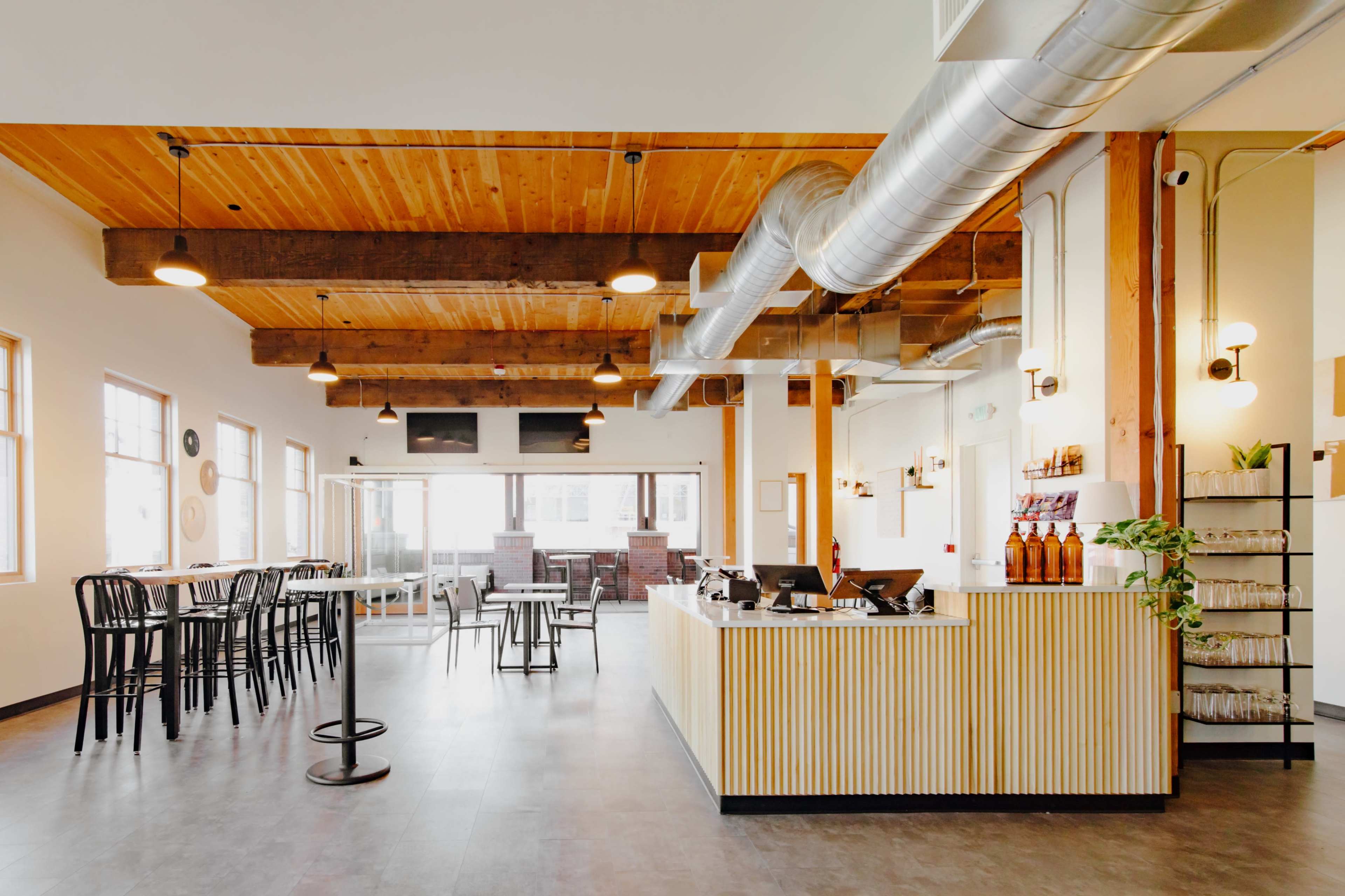 A modern café interior with wooden beams, a counter displaying beverages, and a mix of seating options, including high tables and chairs.