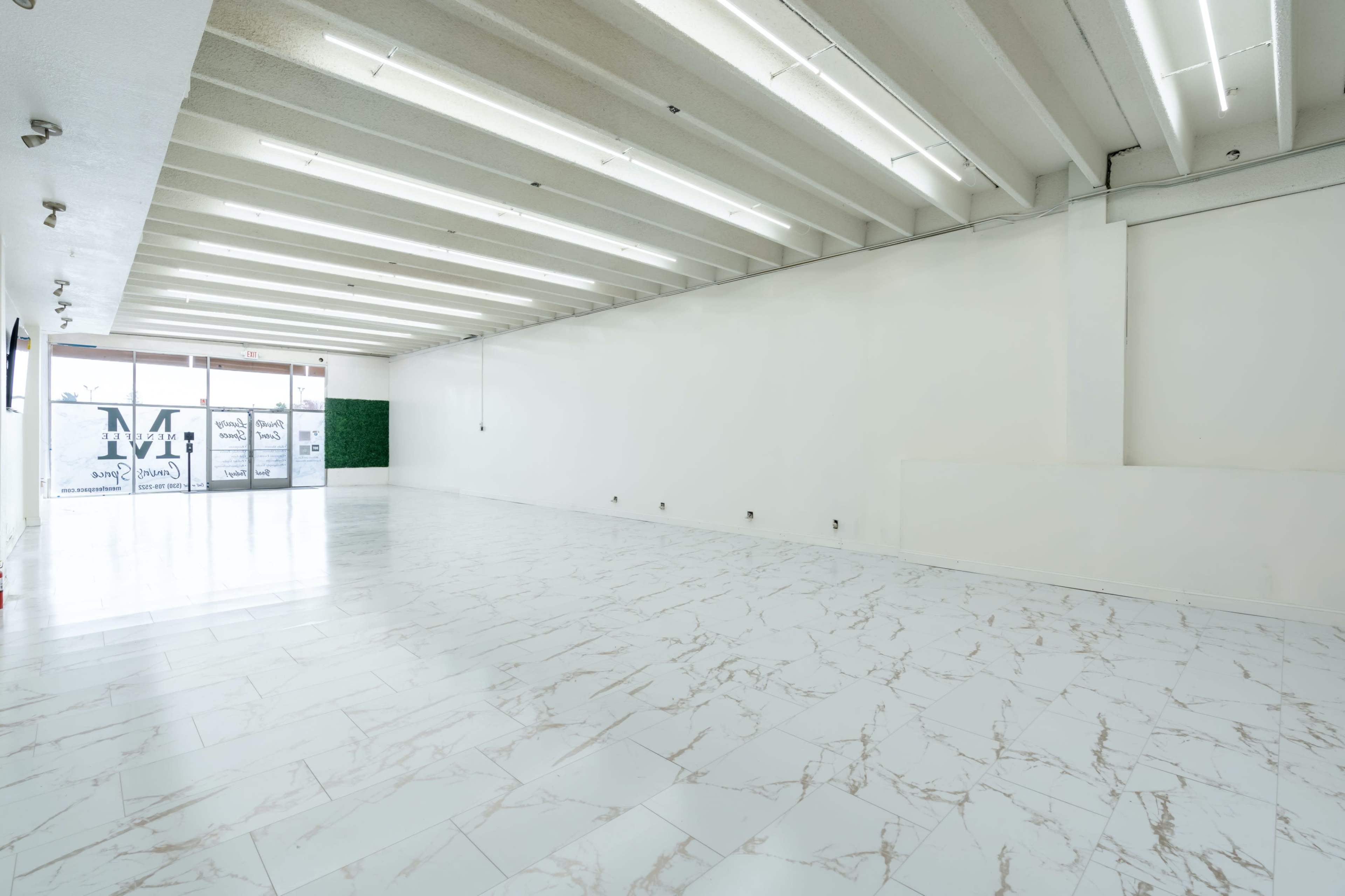 A spacious, empty interior with white walls, a marble-patterned floor, and large windows at the front.