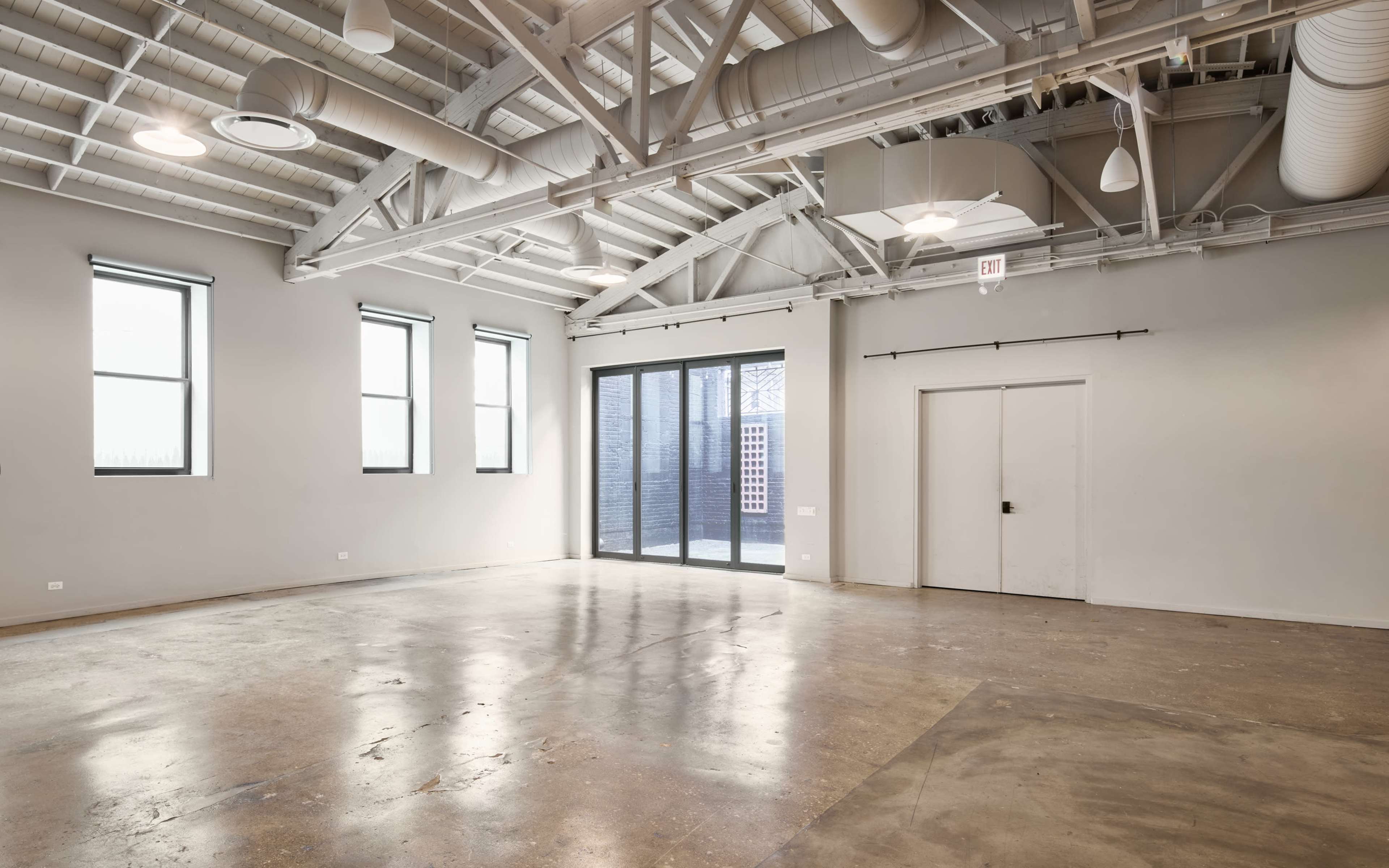 The image shows a spacious, empty room with large windows, polished concrete floors, and exposed ceiling beams.