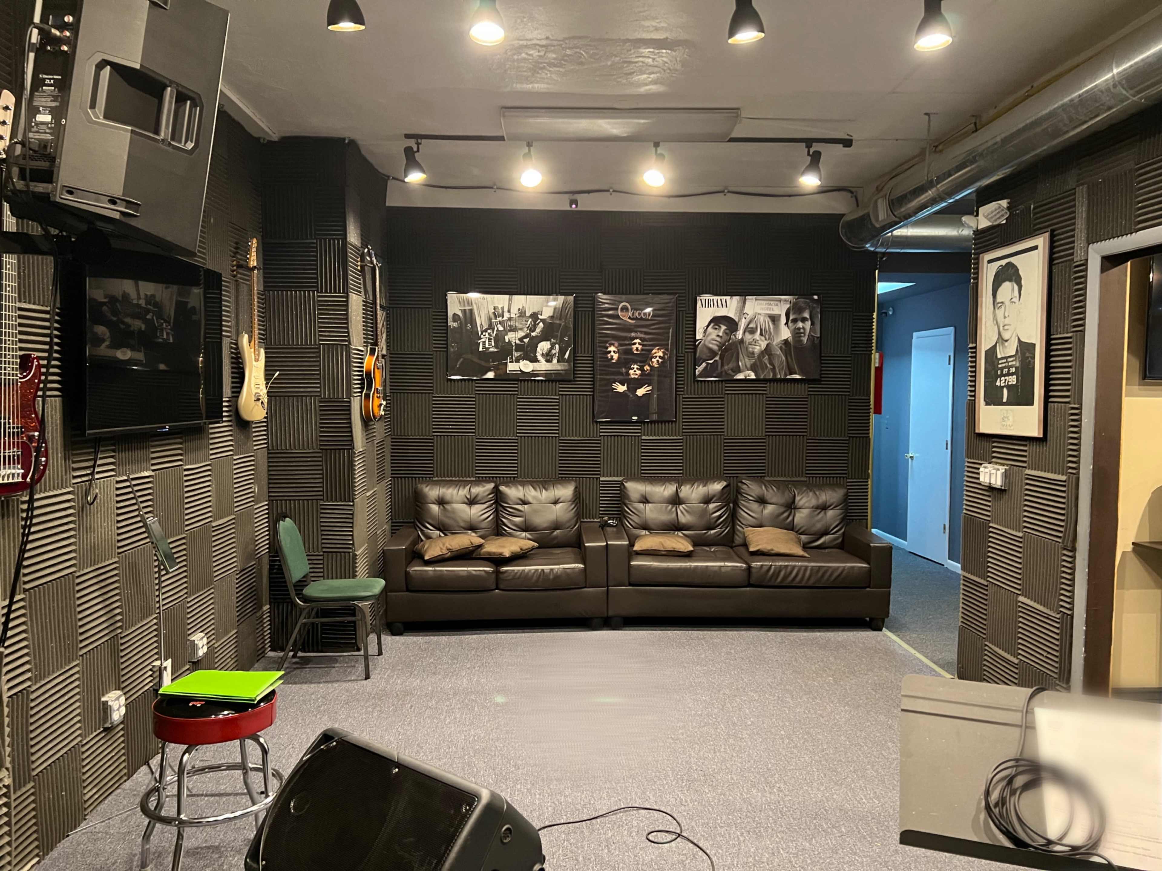 A music rehearsal space featuring a black couch, several framed photographs on the wall, and various musical instruments displayed.