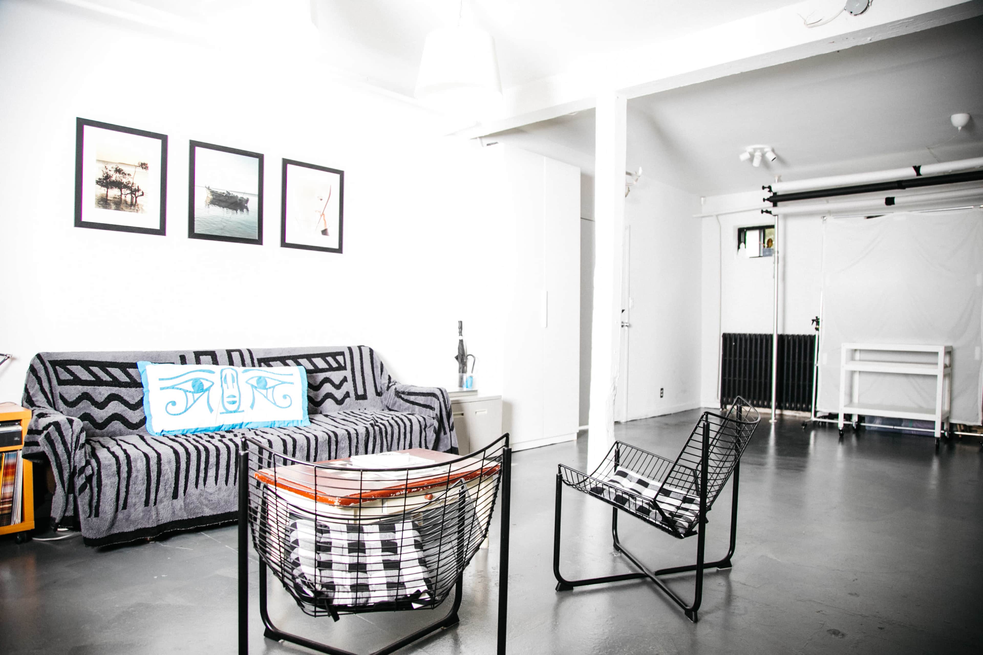 The image shows a modern living room with a gray sofa, two black wire chairs, and minimalist decor, including framed artwork on the walls.
