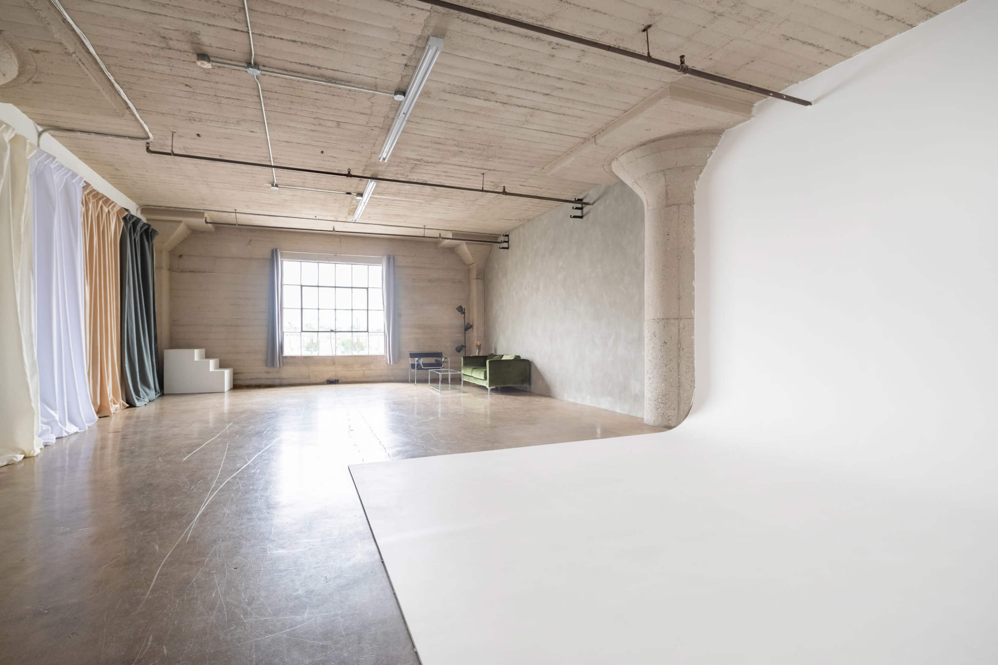 A spacious interior studio features a large window, soft furnishings, and a plain white backdrop.