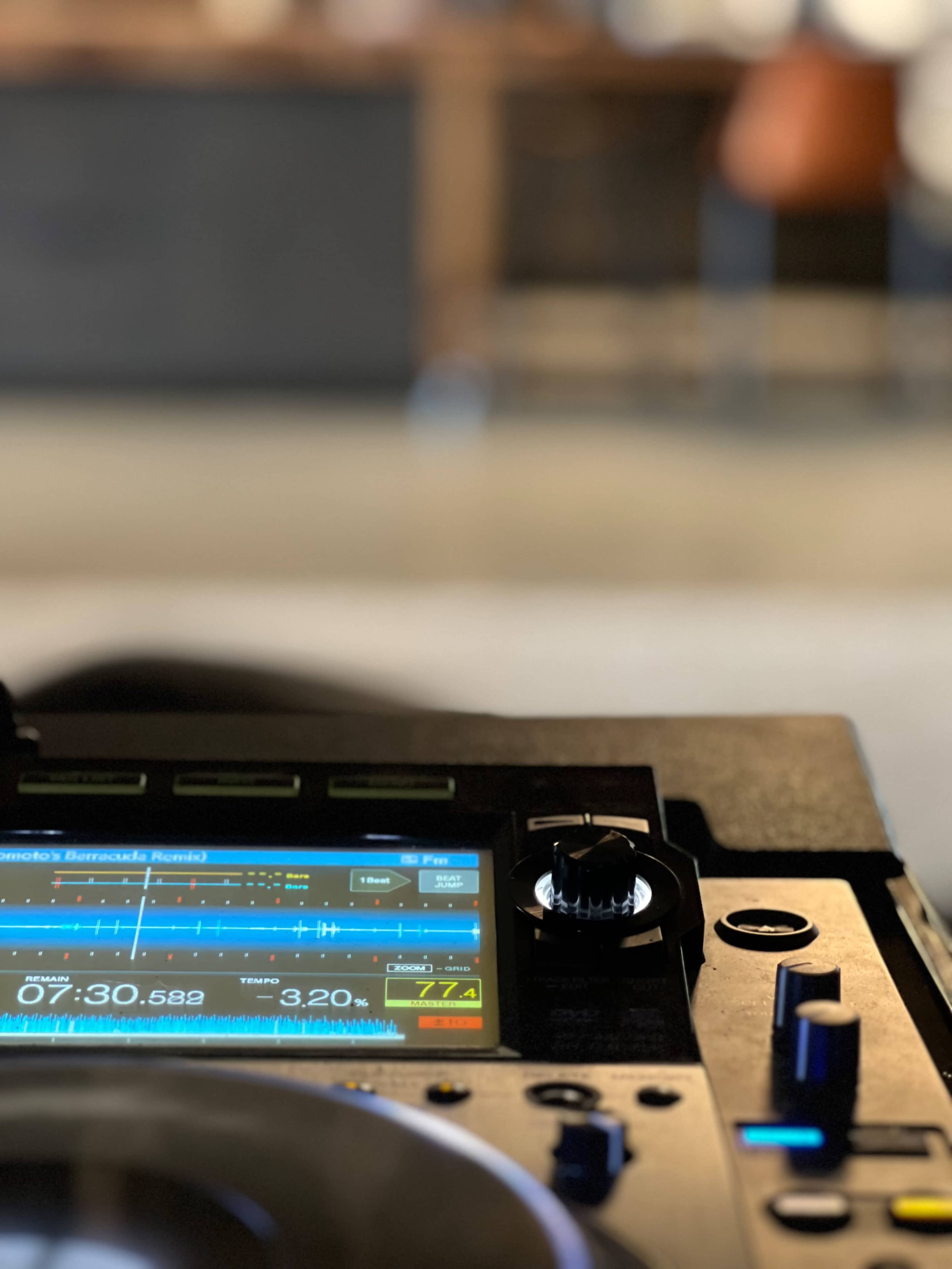 A close-up view of a DJ turntable with a digital display, set against a blurred background of a modern space.