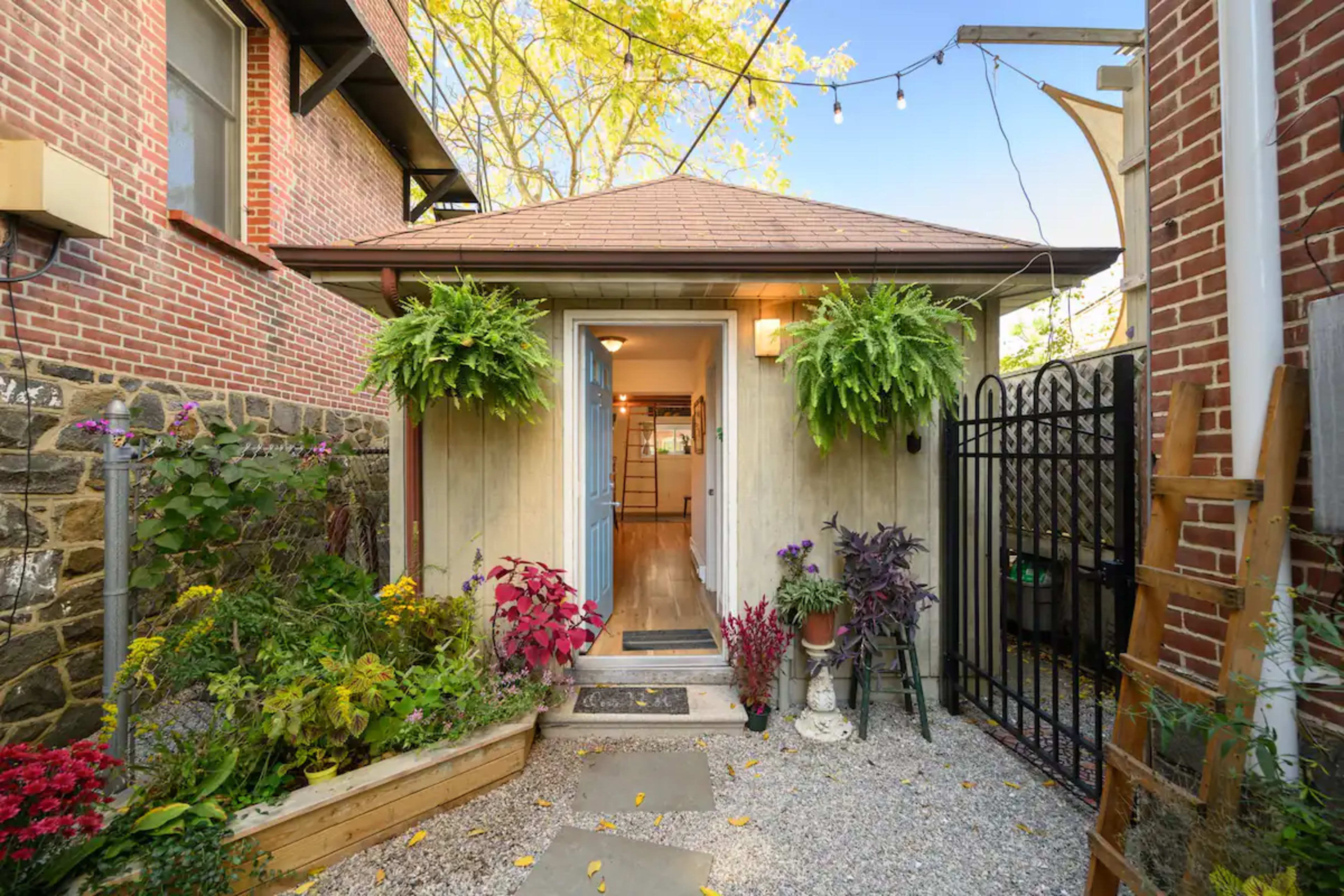 A charming entryway with a pathway leading to a door flanked by hanging plants and surrounded by a gravel garden.