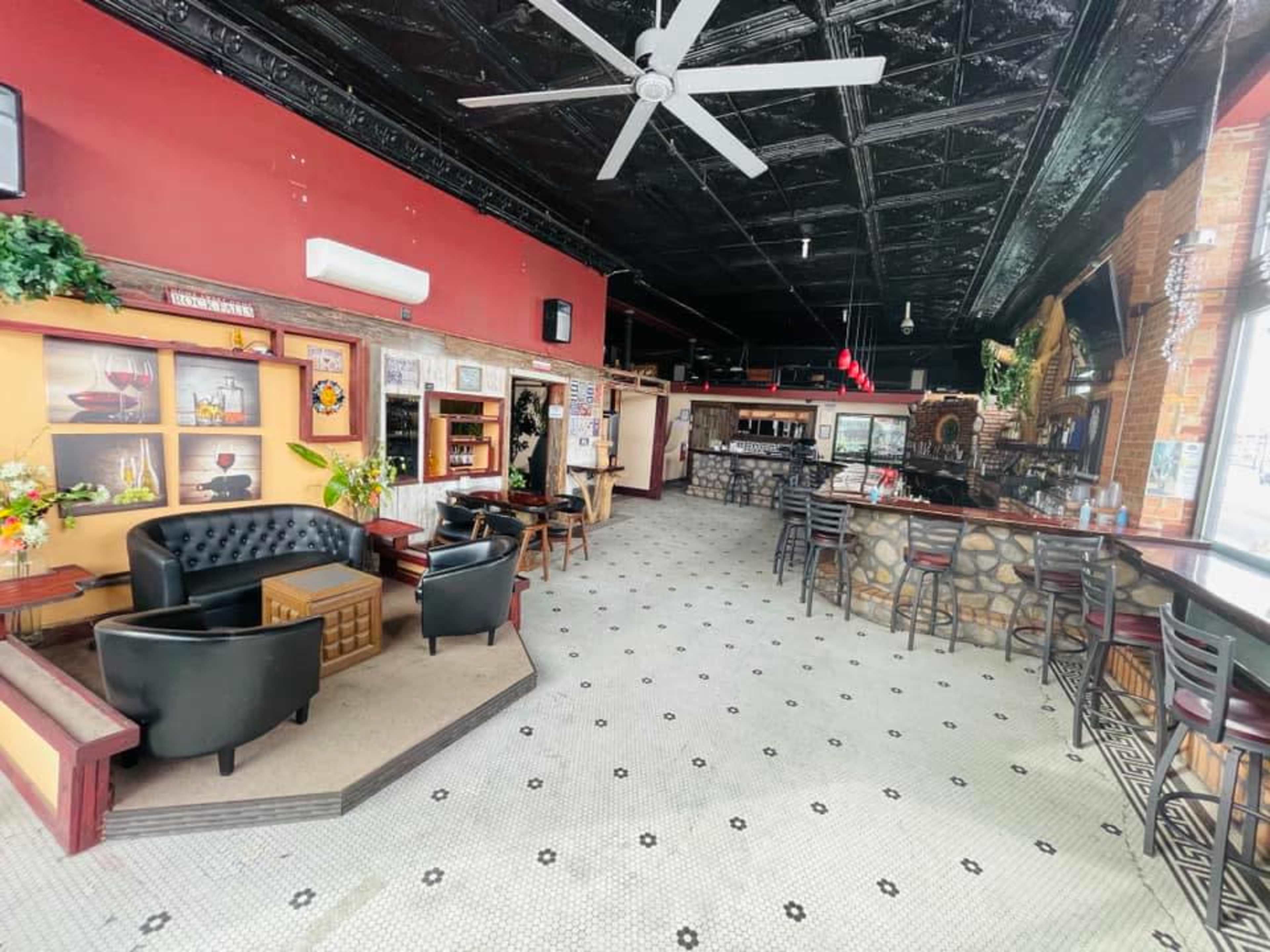 The interior of a restaurant or bar, featuring black leather seating, a stone bar counter, and a tiled floor with a ceiling fan overhead.