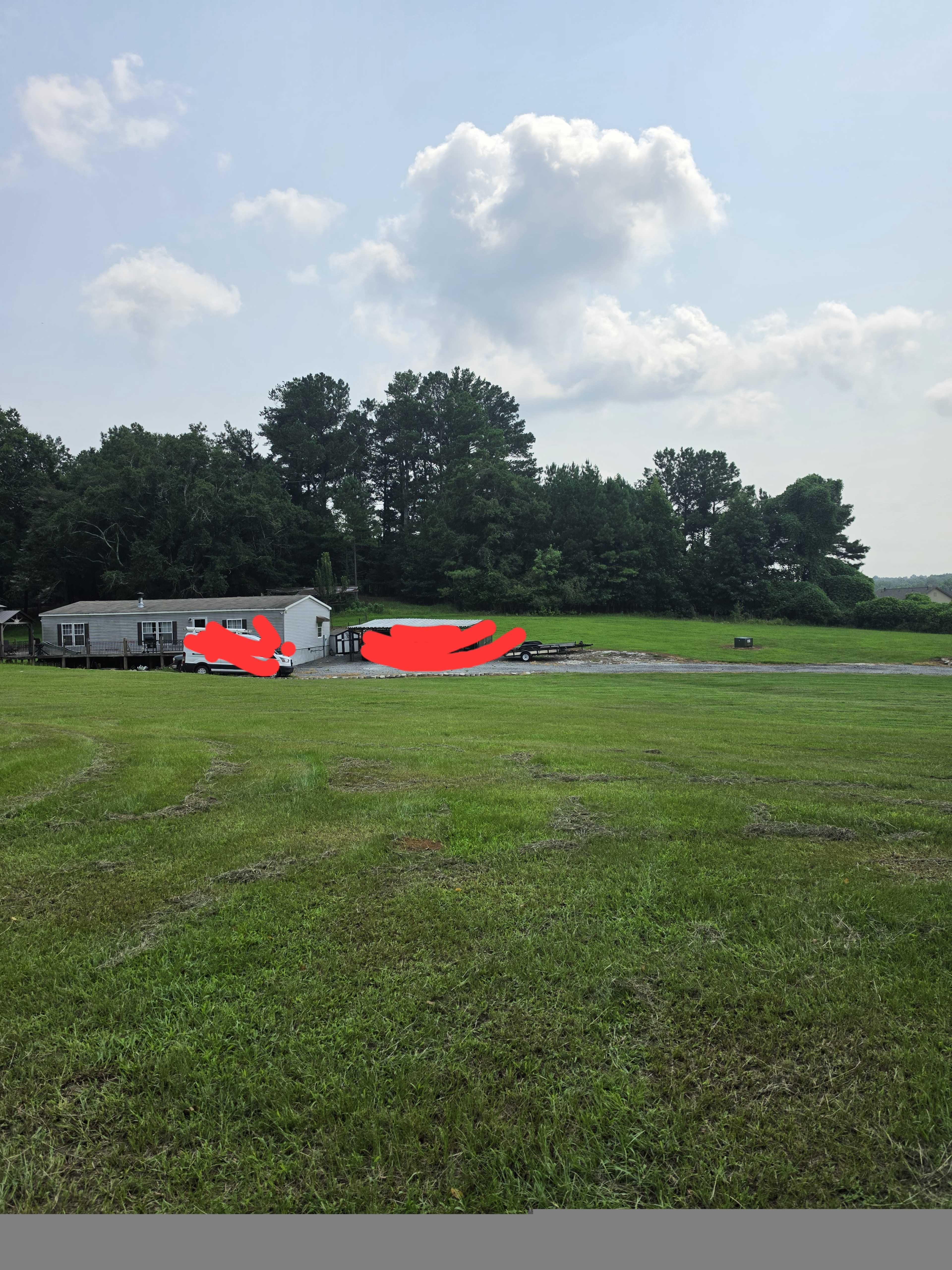 A grassy lawn extends towards a house and several vehicles in the background, with trees lining the horizon under a partly cloudy sky.