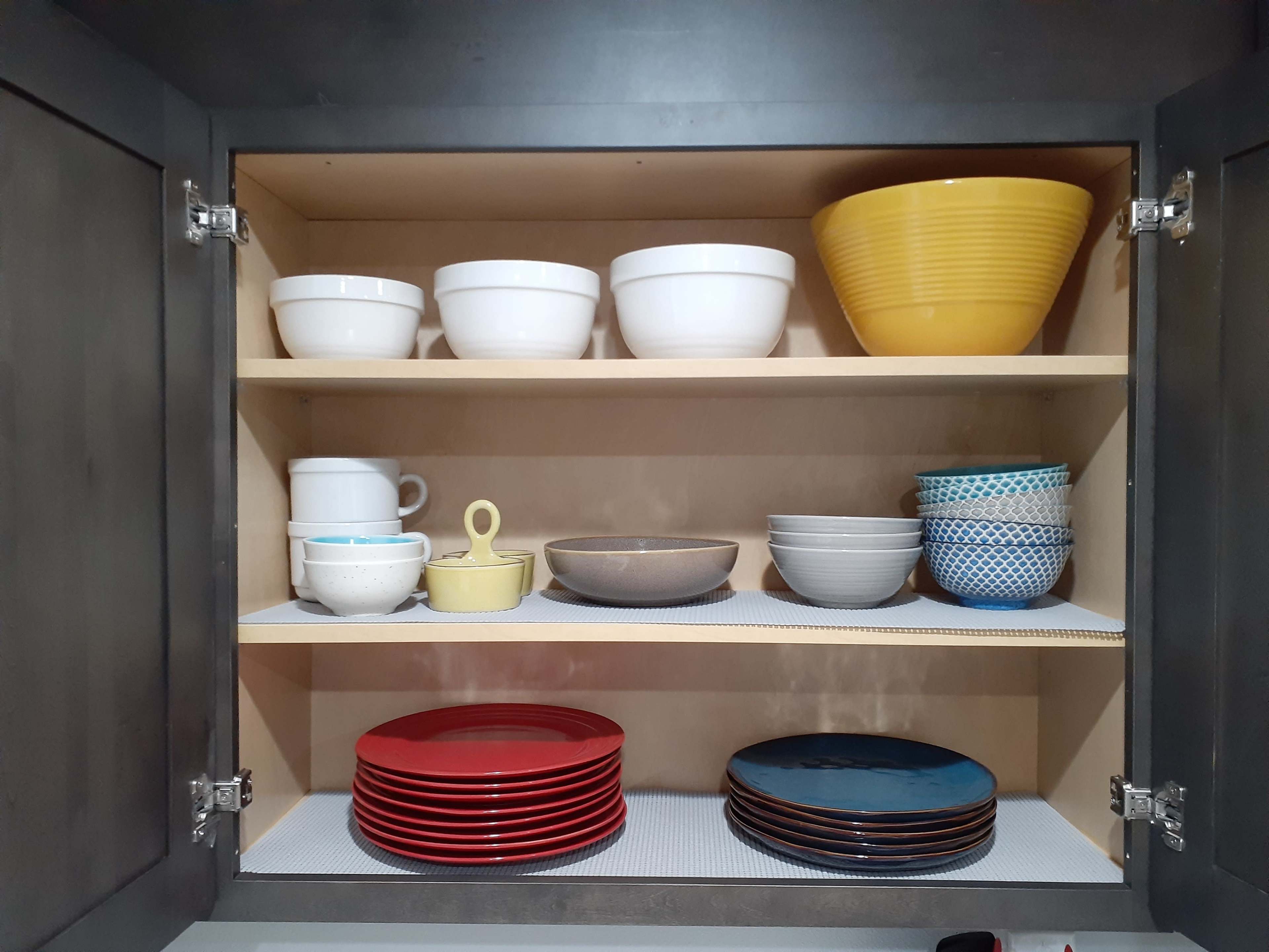 A kitchen cabinet with multiple shelves containing a variety of bowls, plates, and cups organized neatly.