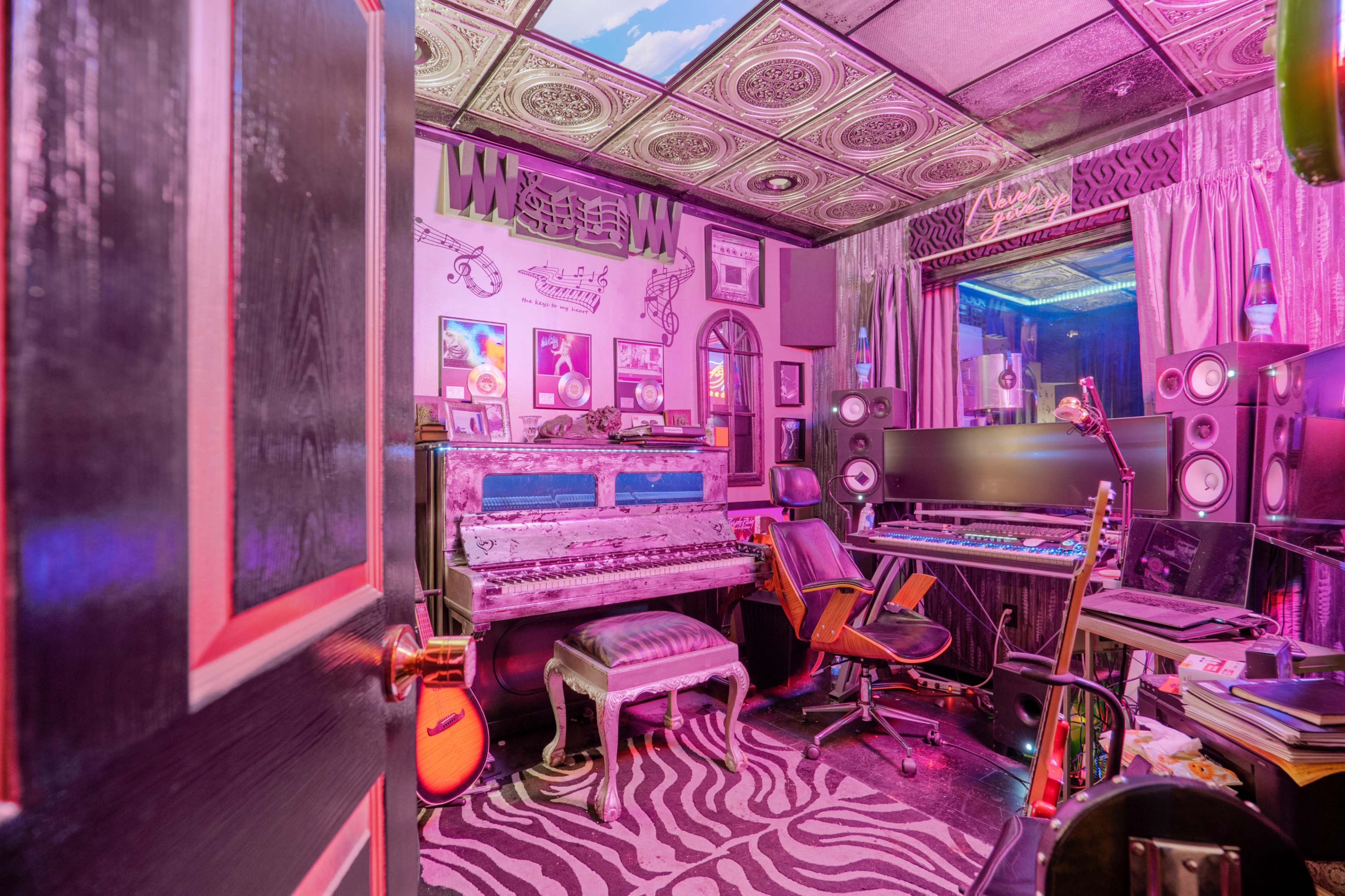 A colorful music studio featuring a vintage piano, recording equipment, and eclectic decor, all illuminated by vibrant lighting.