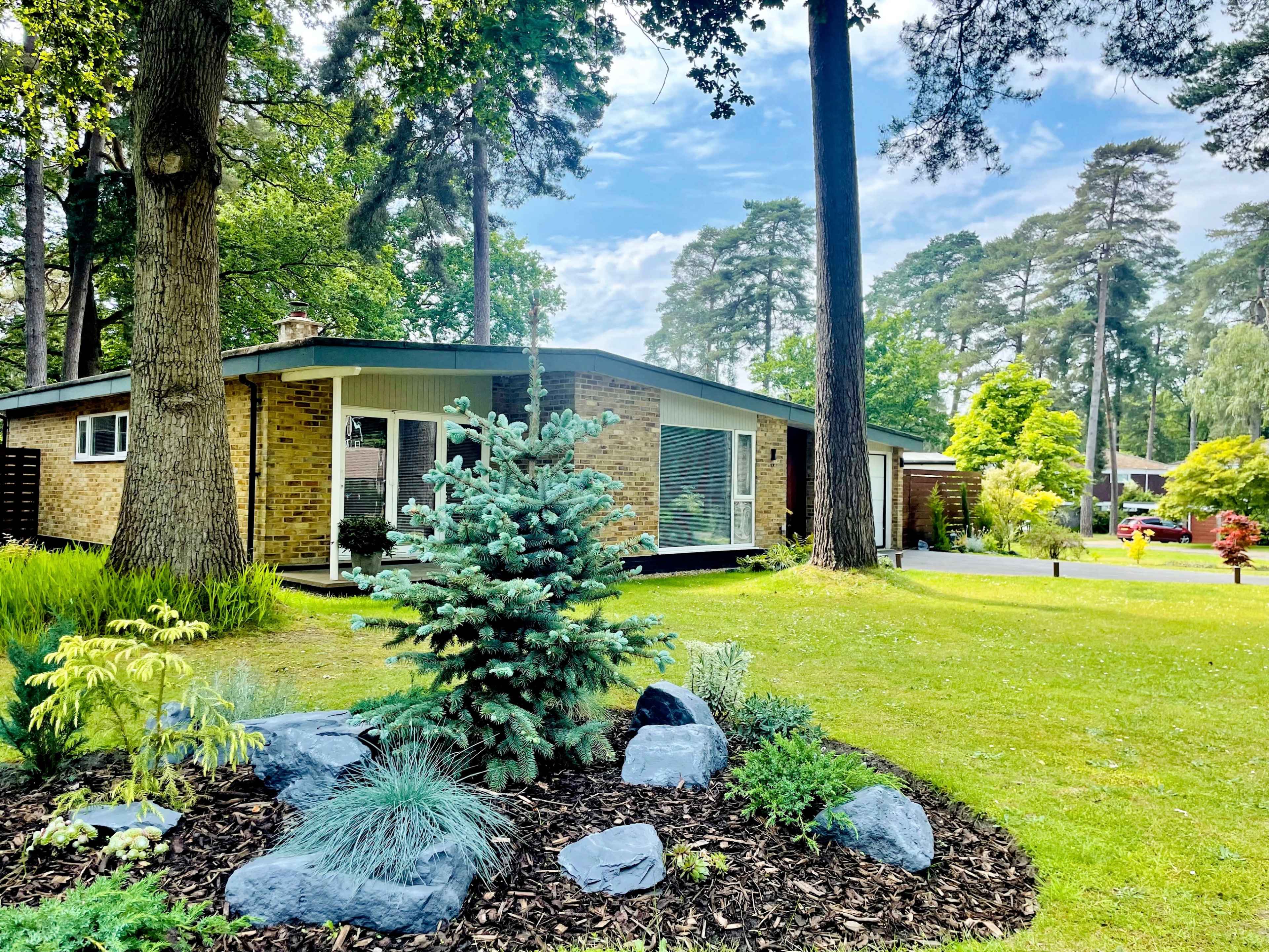 A modern single-story house is surrounded by landscaped gardens, featuring a mix of trees and ornamental plants.