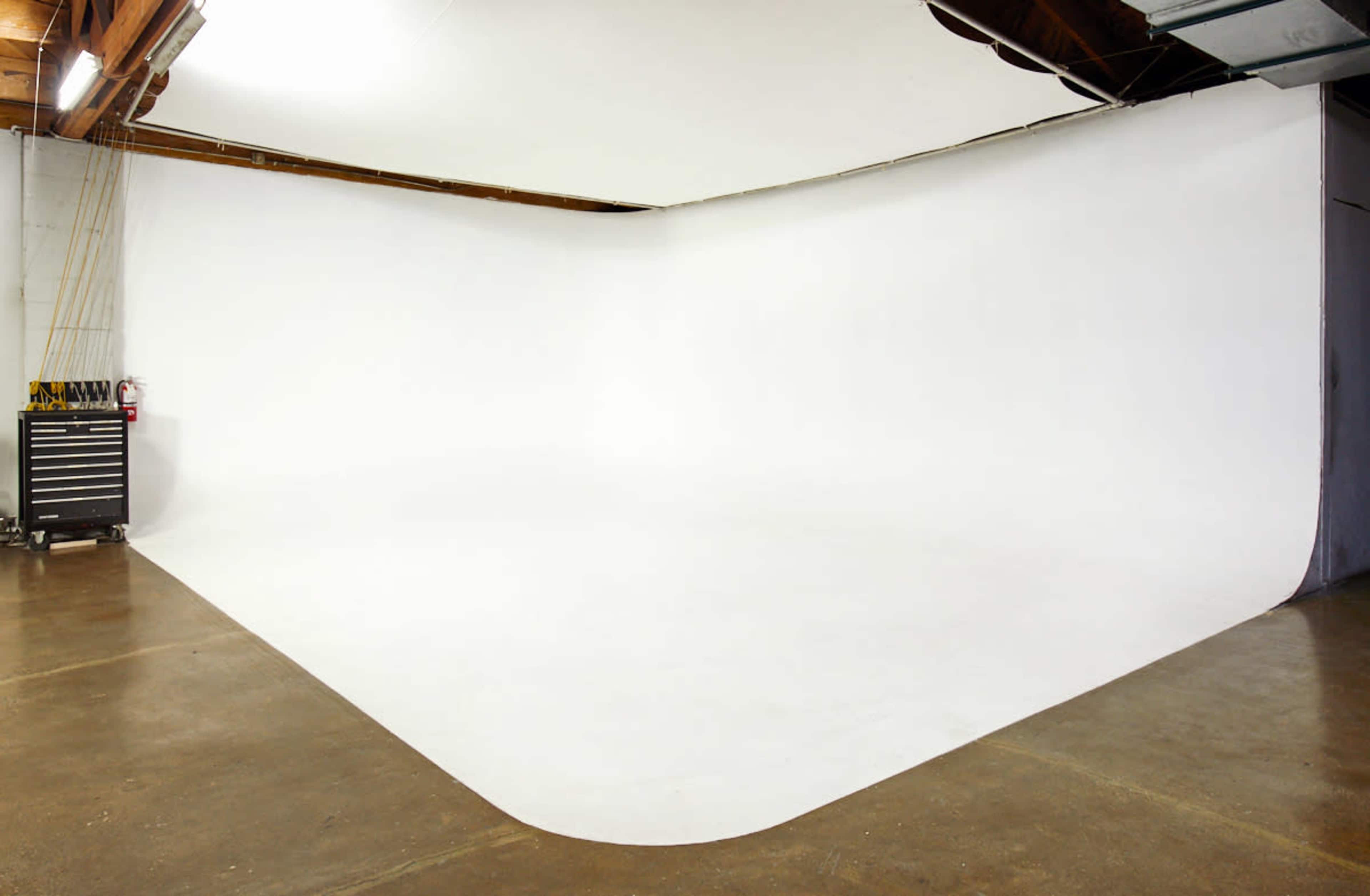 A spacious photography studio with a white seamless backdrop and a concrete floor.