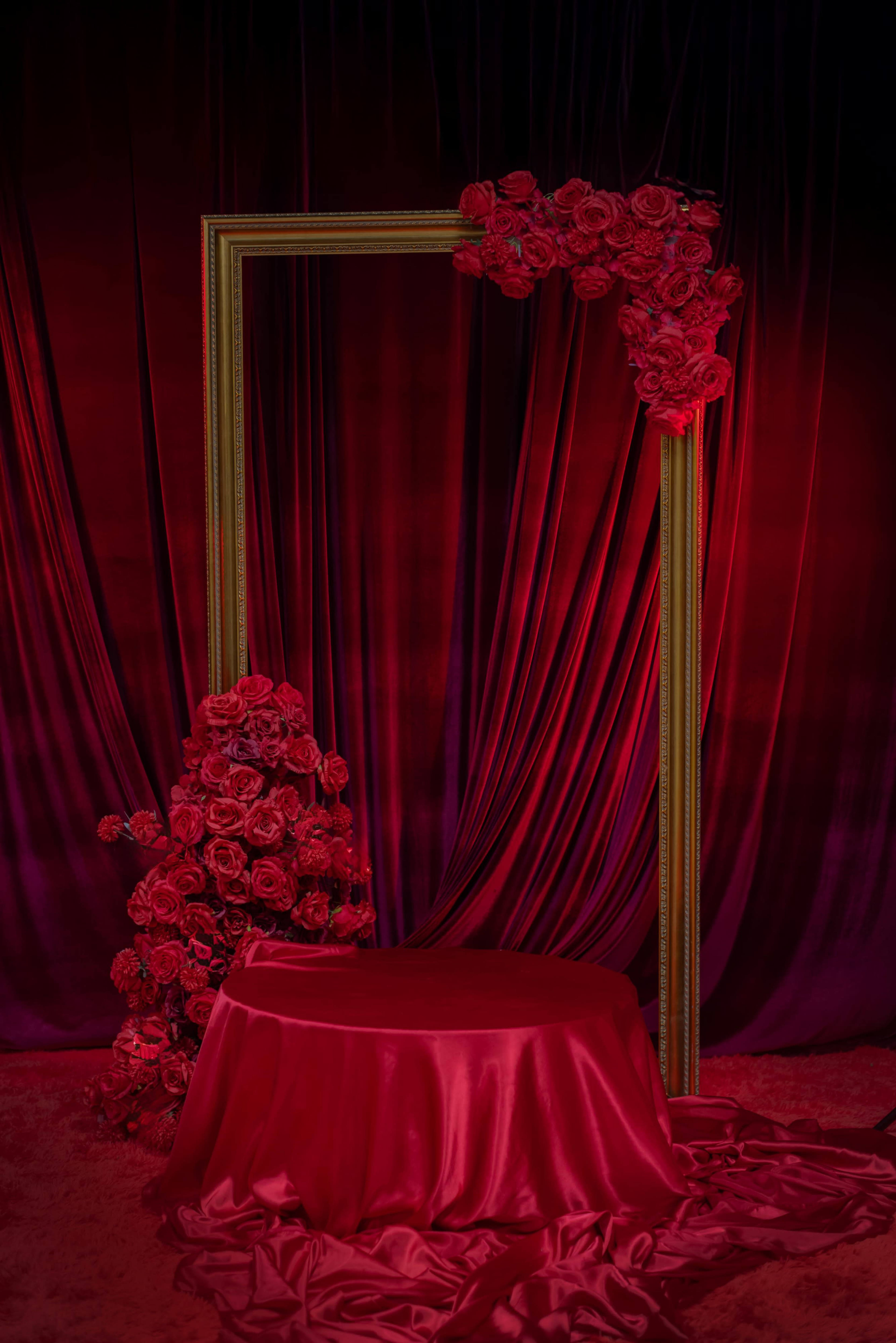 The scene features a tall decorative frame adorned with red roses, set against a backdrop of deep red, draped fabric.