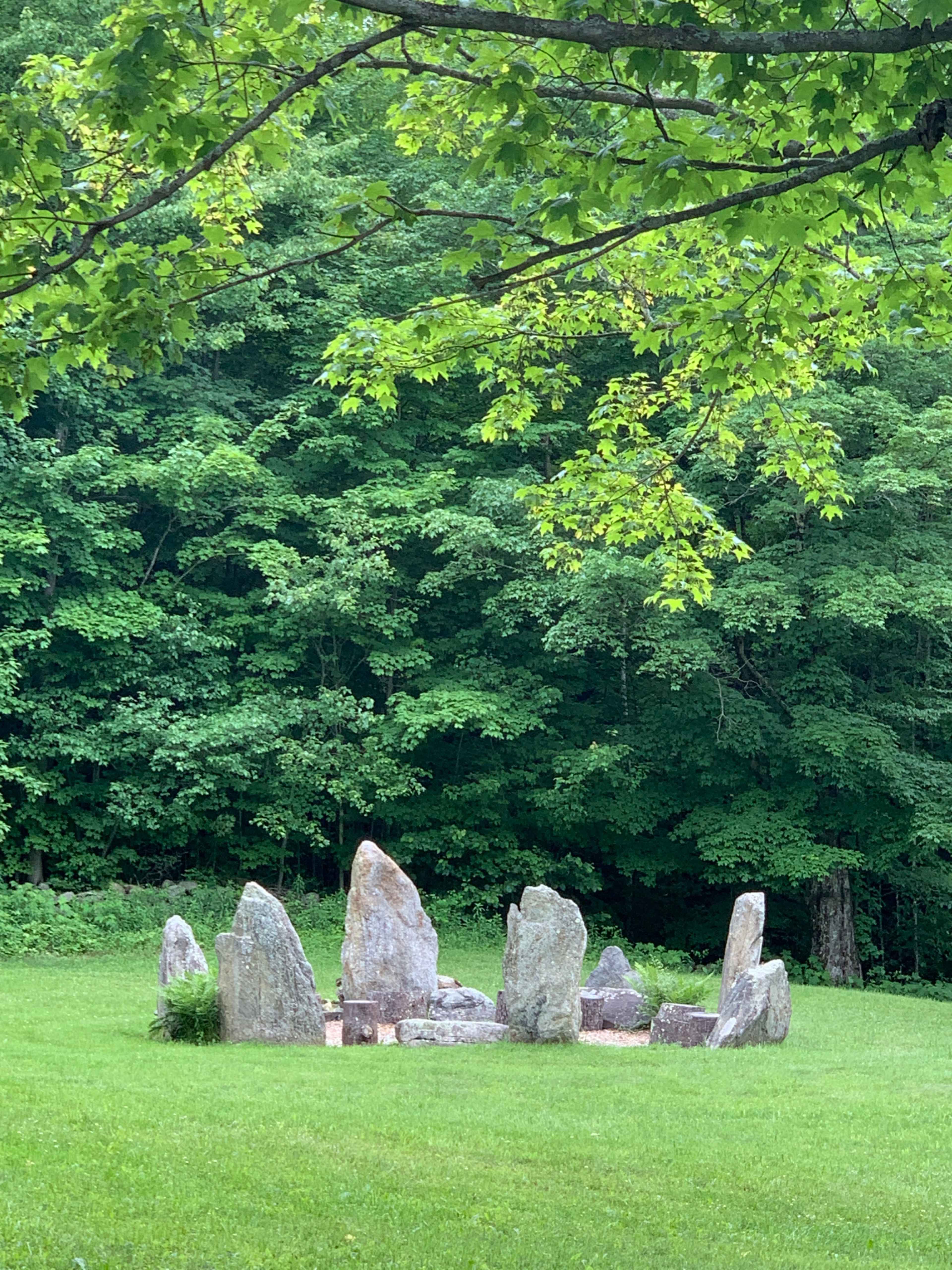 A circle of upright stones set in a grassy area surrounded by dense trees.