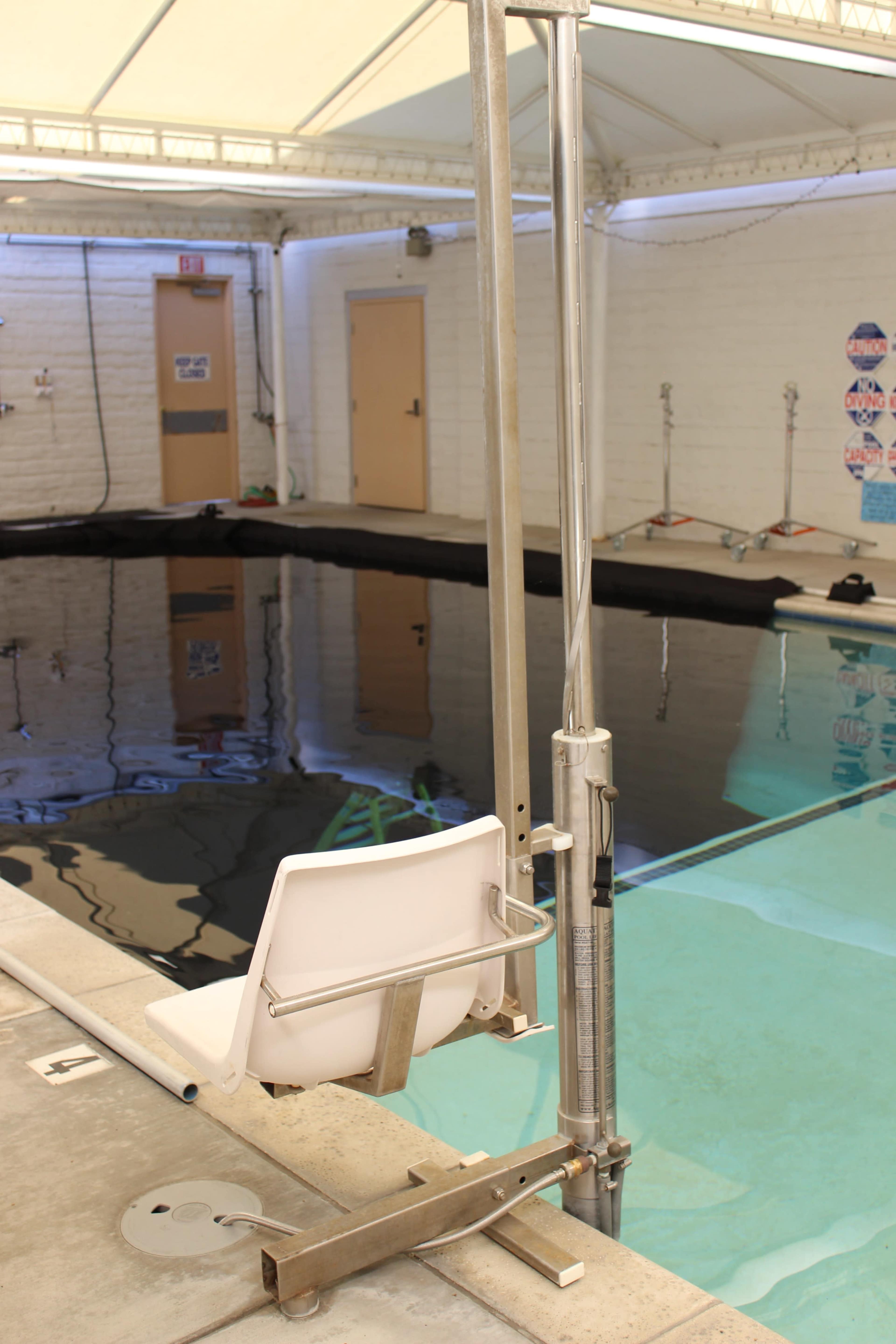 A swimming pool with a sloped entry and a mechanical lift chair positioned next to the water's edge.