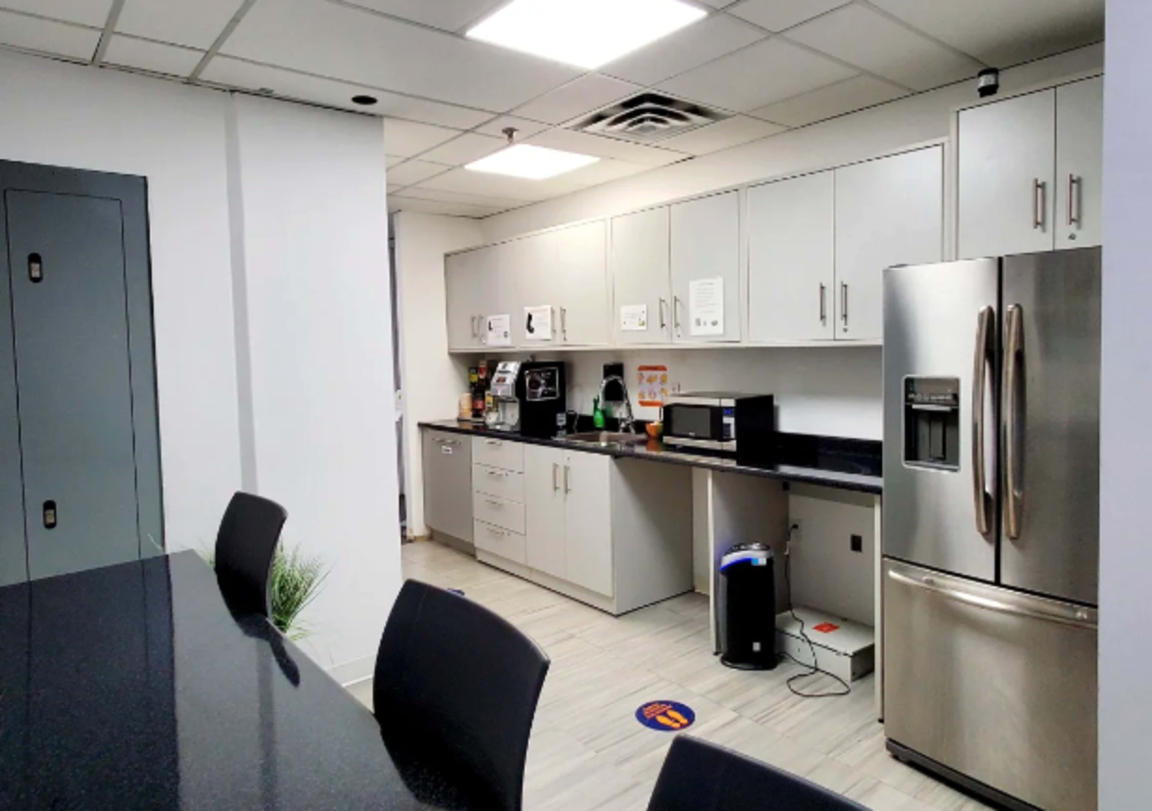 A modern kitchen area with gray cabinets, a stainless steel refrigerator, and a countertop equipped with appliances like a microwave and coffee maker.