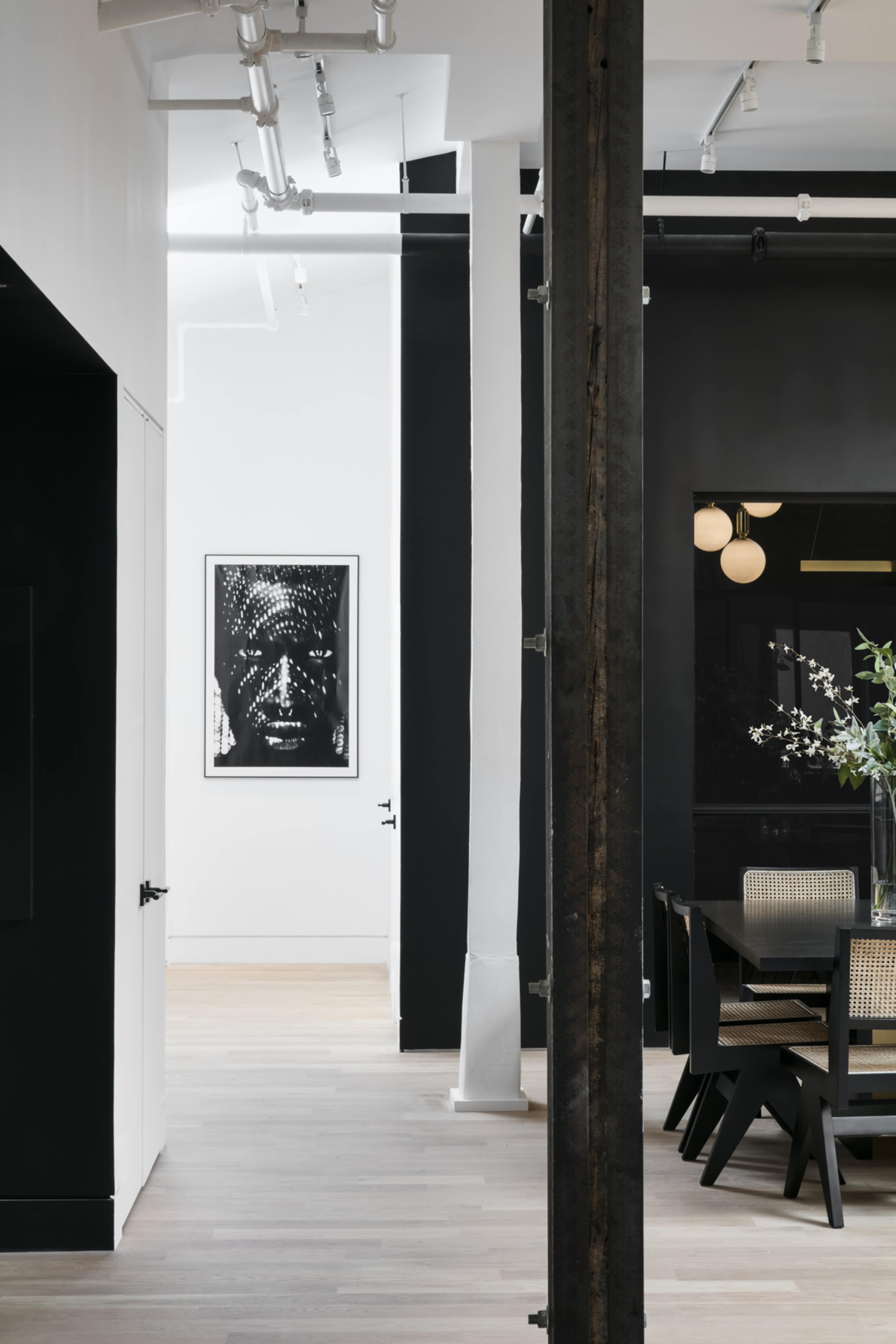 A minimalistic interior space featuring a black and white art piece on the wall, a dining area with a wooden table and chairs, and contrasting white and black walls.