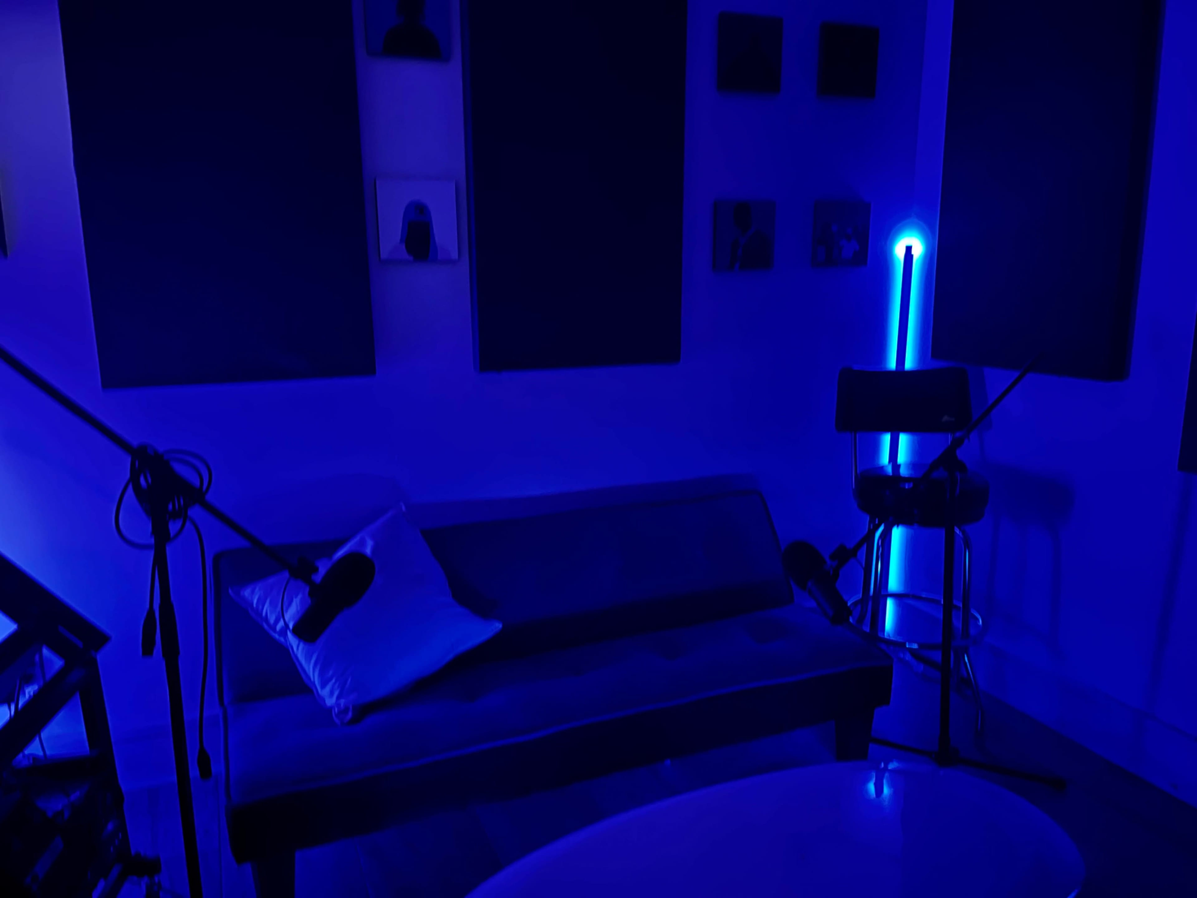 A blue-lit room features a couch, a bar stool with a neon light, and soundproofing panels on the walls.