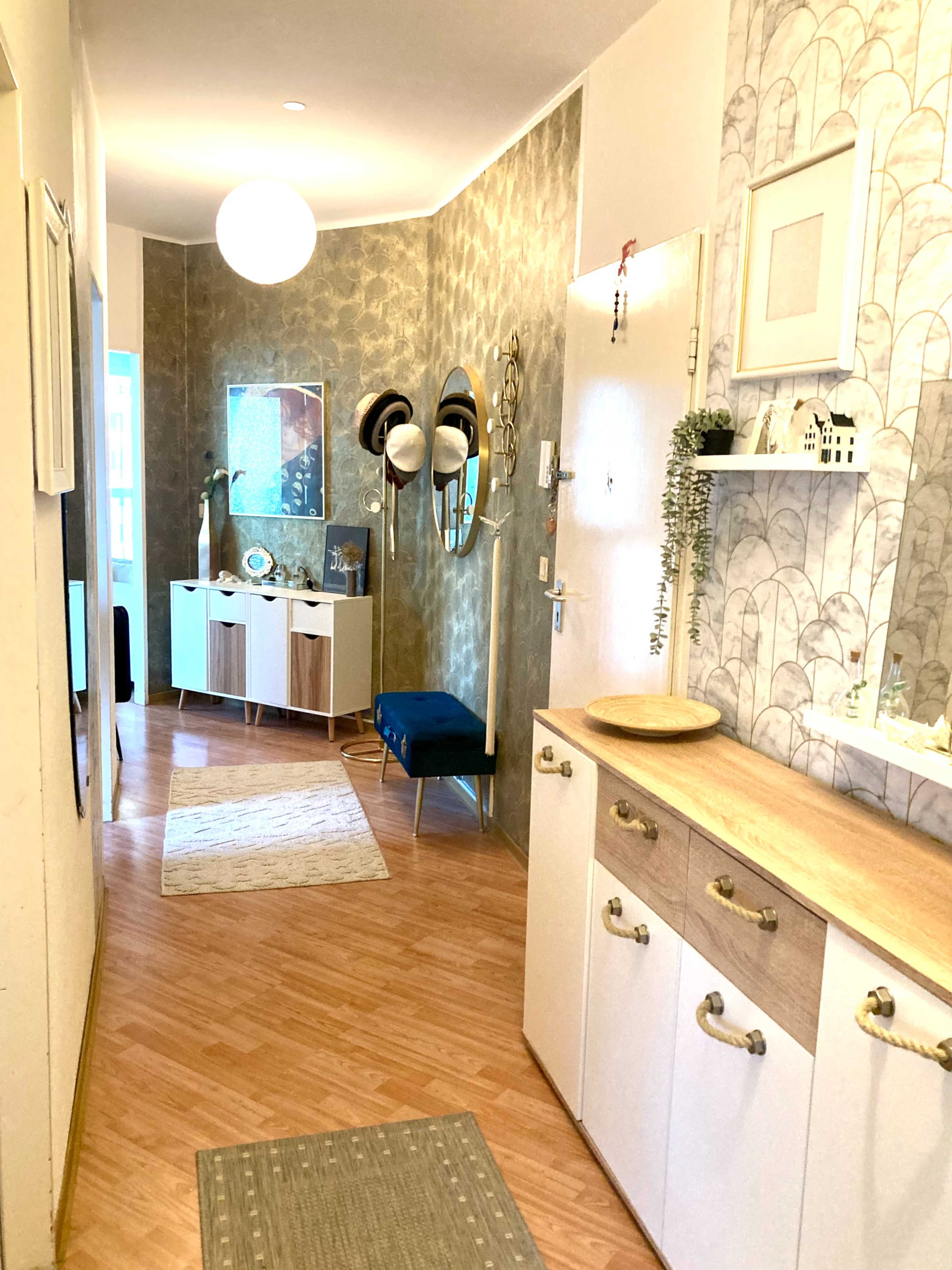 The image shows a decorated hallway featuring a console table with drawers, a blue bench, and framed artwork on the walls.