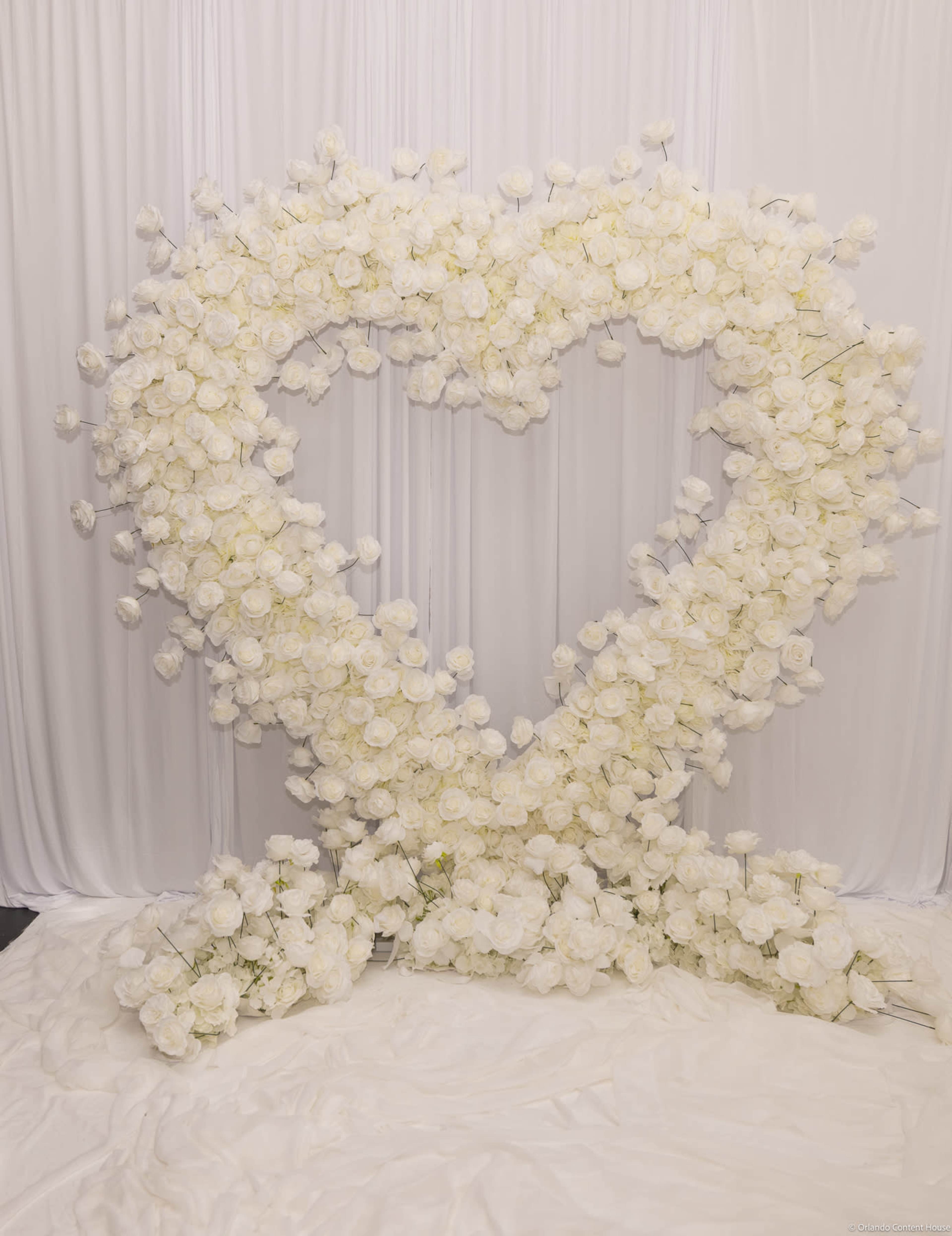 A large heart-shaped installation made of white roses is displayed against a white backdrop.