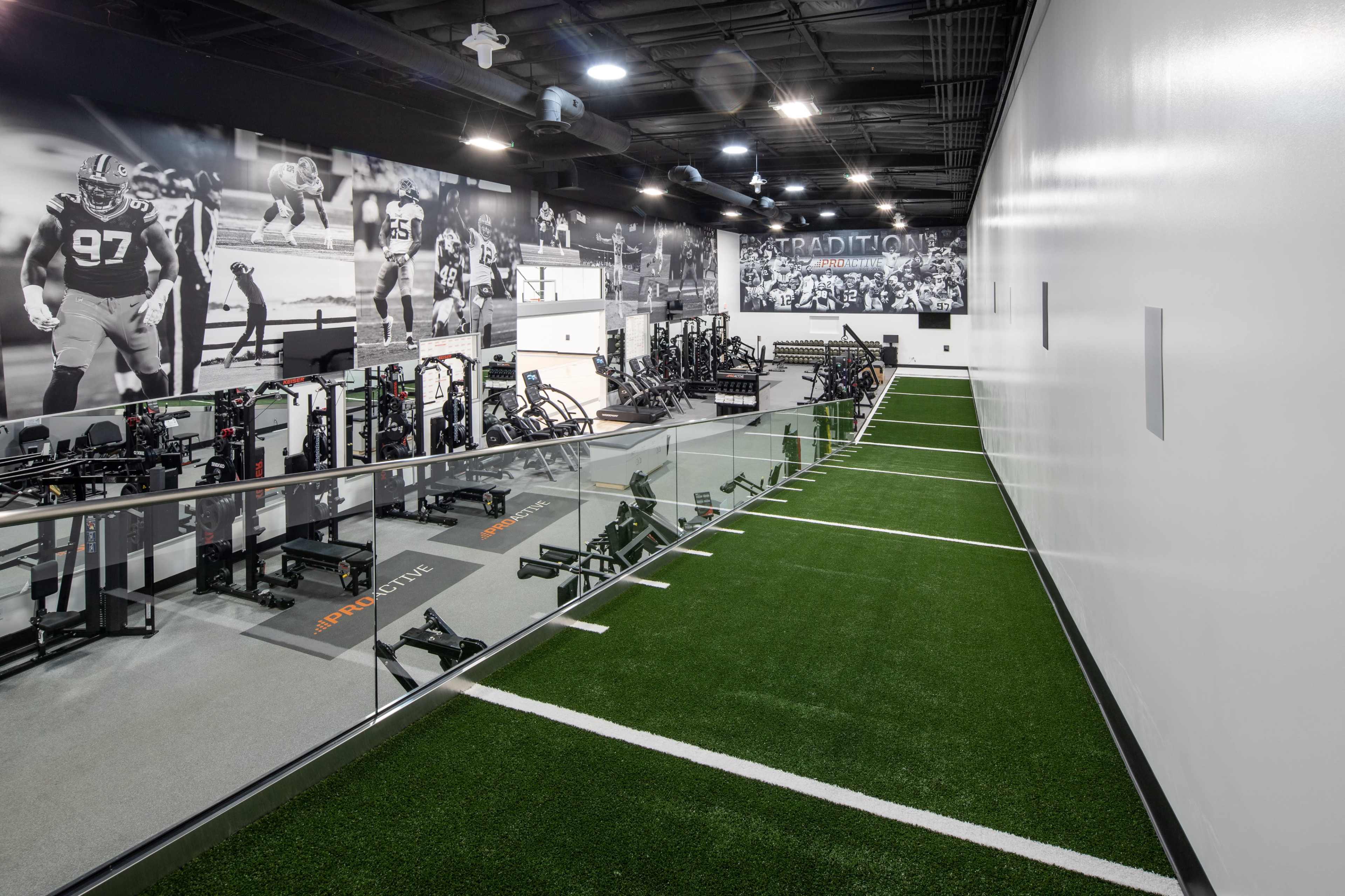 The image shows a modern training facility featuring turf, workout equipment, and large wall murals of athletes.