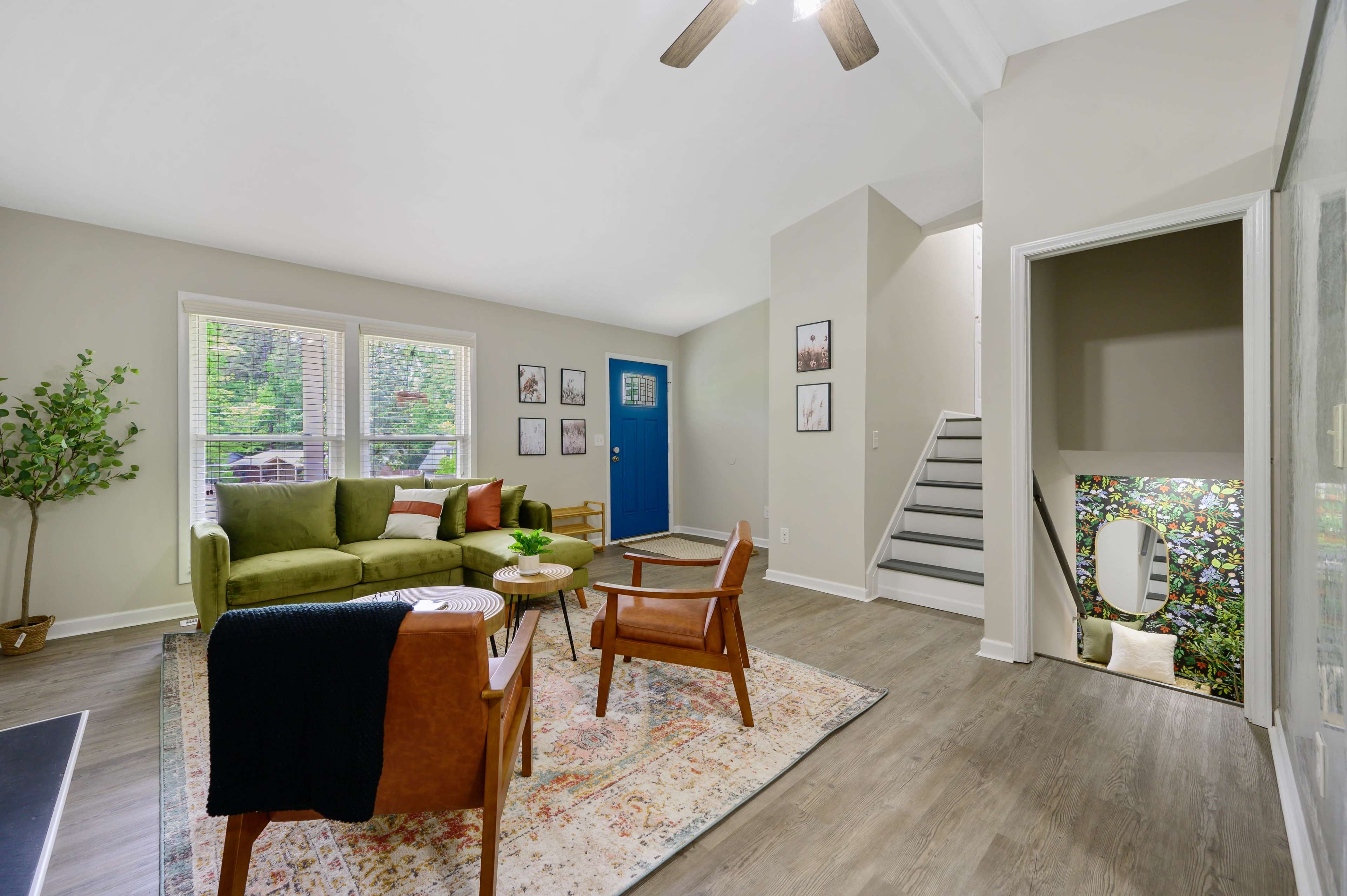 The living room features a green couch, two wooden chairs, a round table, and a blue front door, with stairs leading to a hallway on the right.