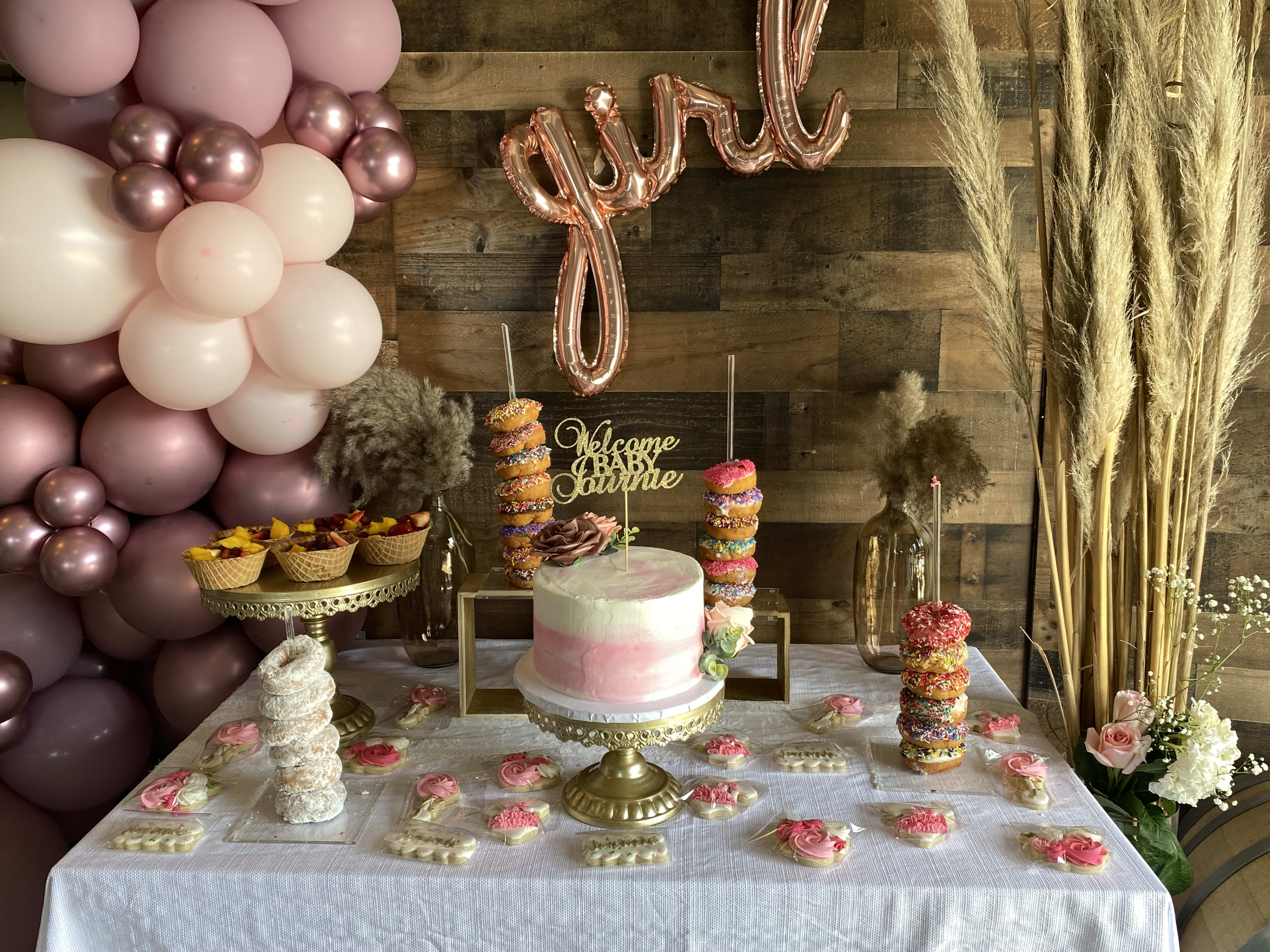 Una mesa de inspiración boho adornada con una tarta rosa rústica y muchos globos, perfecta para la celebración de un baby shower.