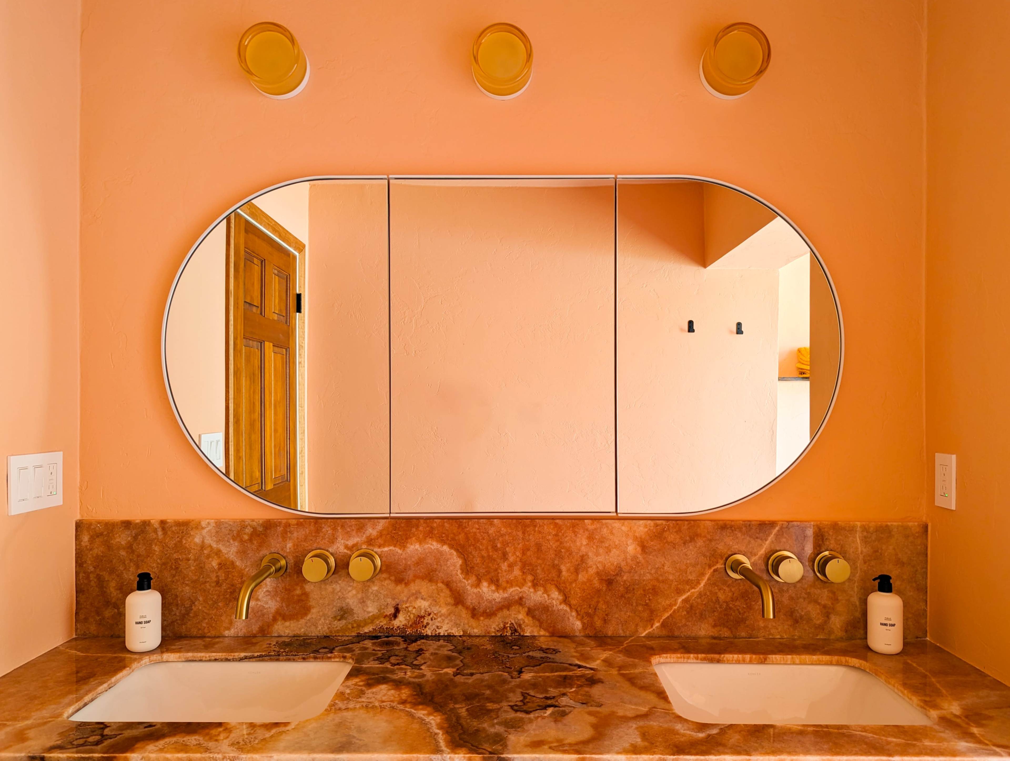 A bathroom vanity with a double sink, a large oval mirror, and warm peach-colored walls.