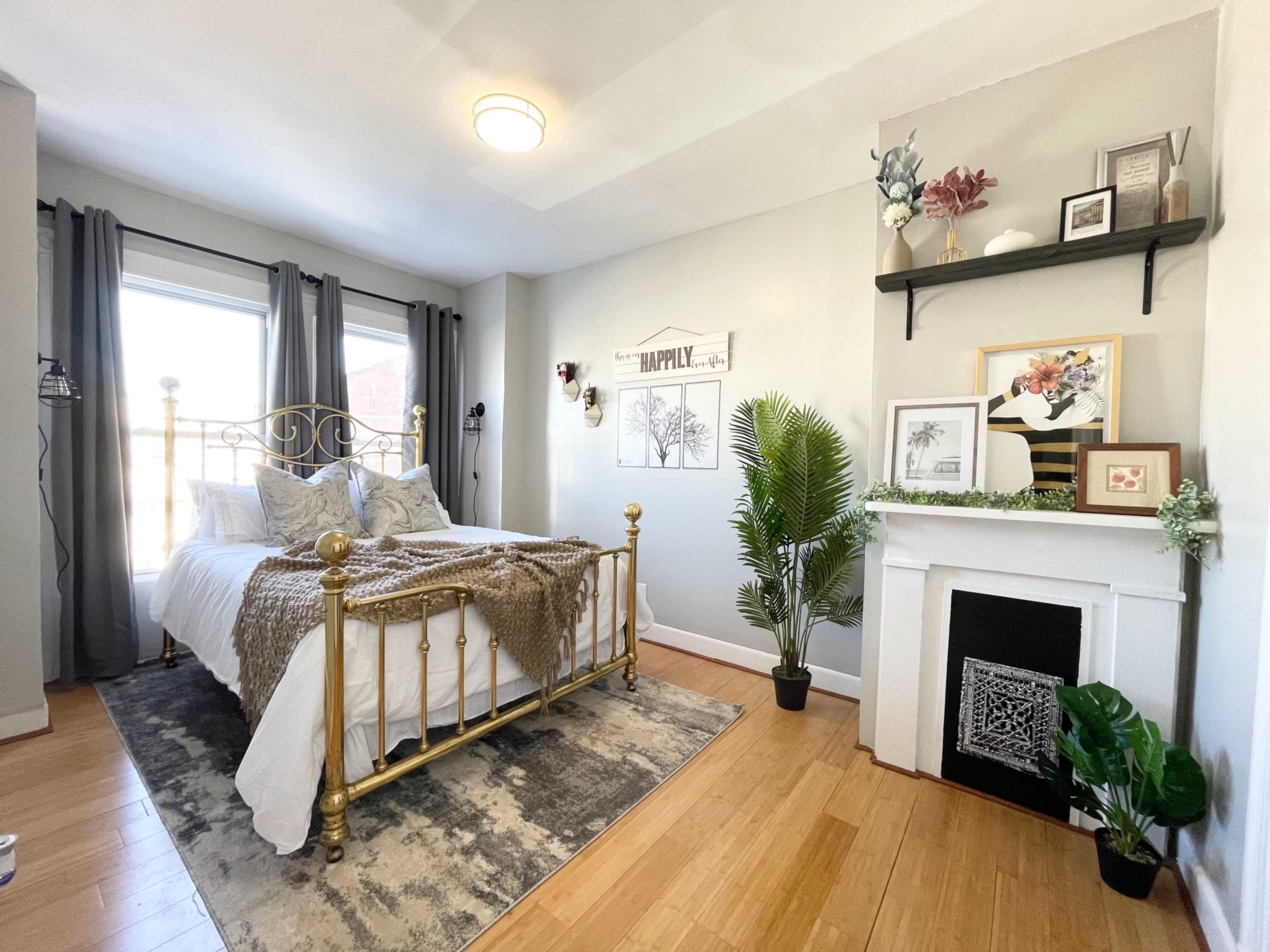 A well-decorated bedroom with a gold bed frame, a patterned rug, and a decorative fireplace, complemented by plants and wall art.