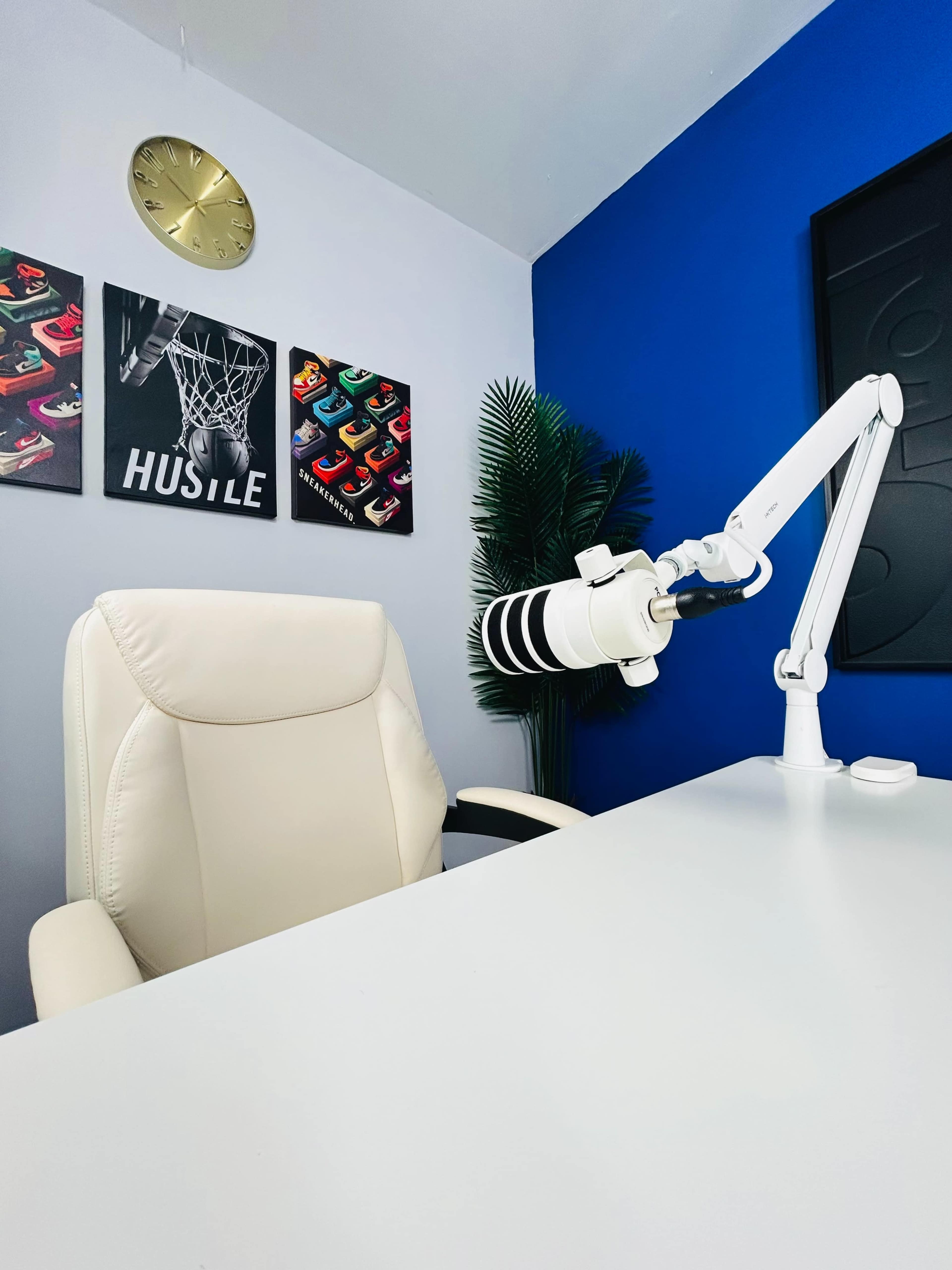 A white office chair sits in front of a white desk, accompanied by a mounted microphone and colorful artwork on the walls.