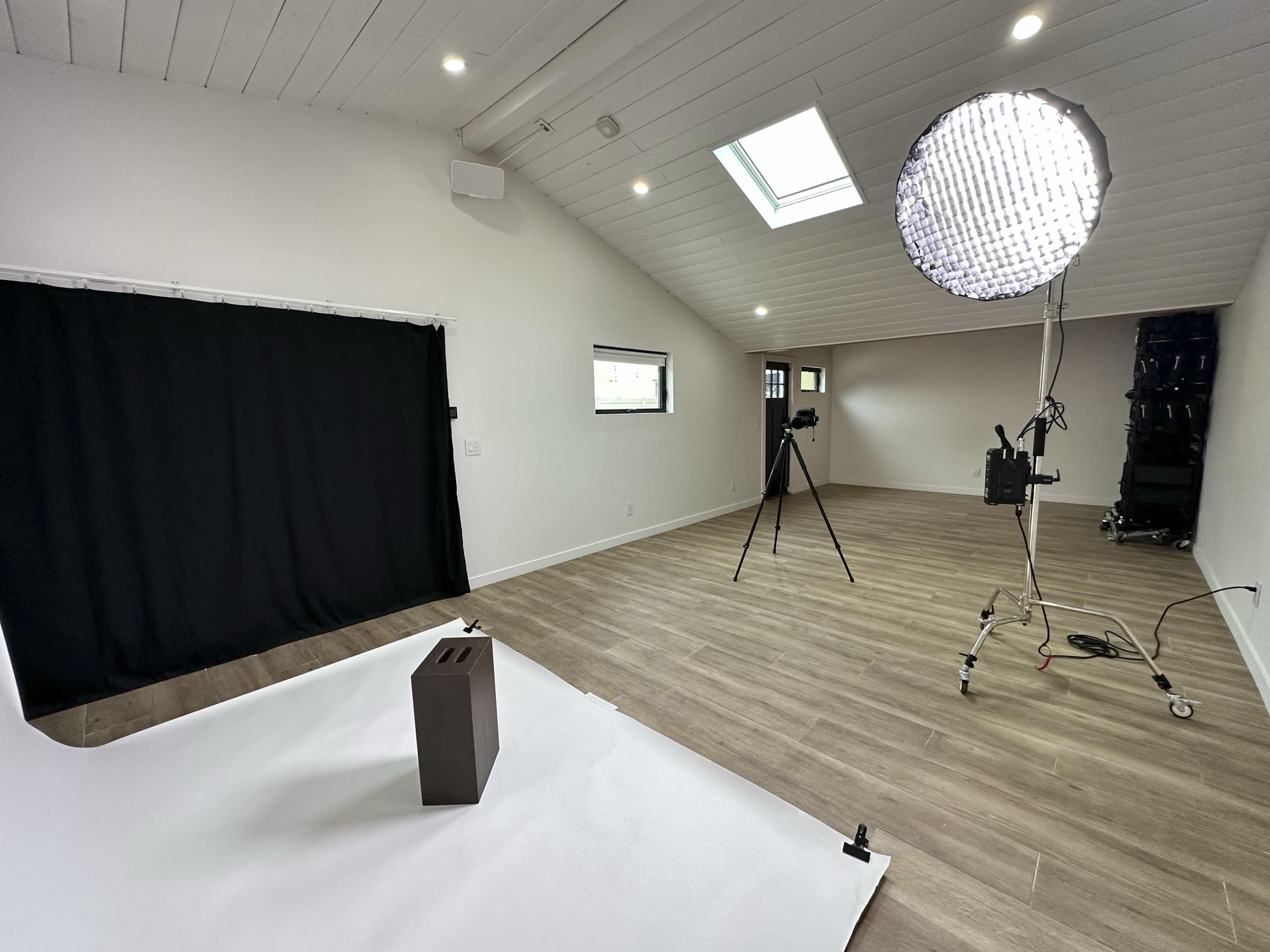 A minimalistic studio setup featuring a dark backdrop, a light source on a stand, and a brown object placed on a white surface.