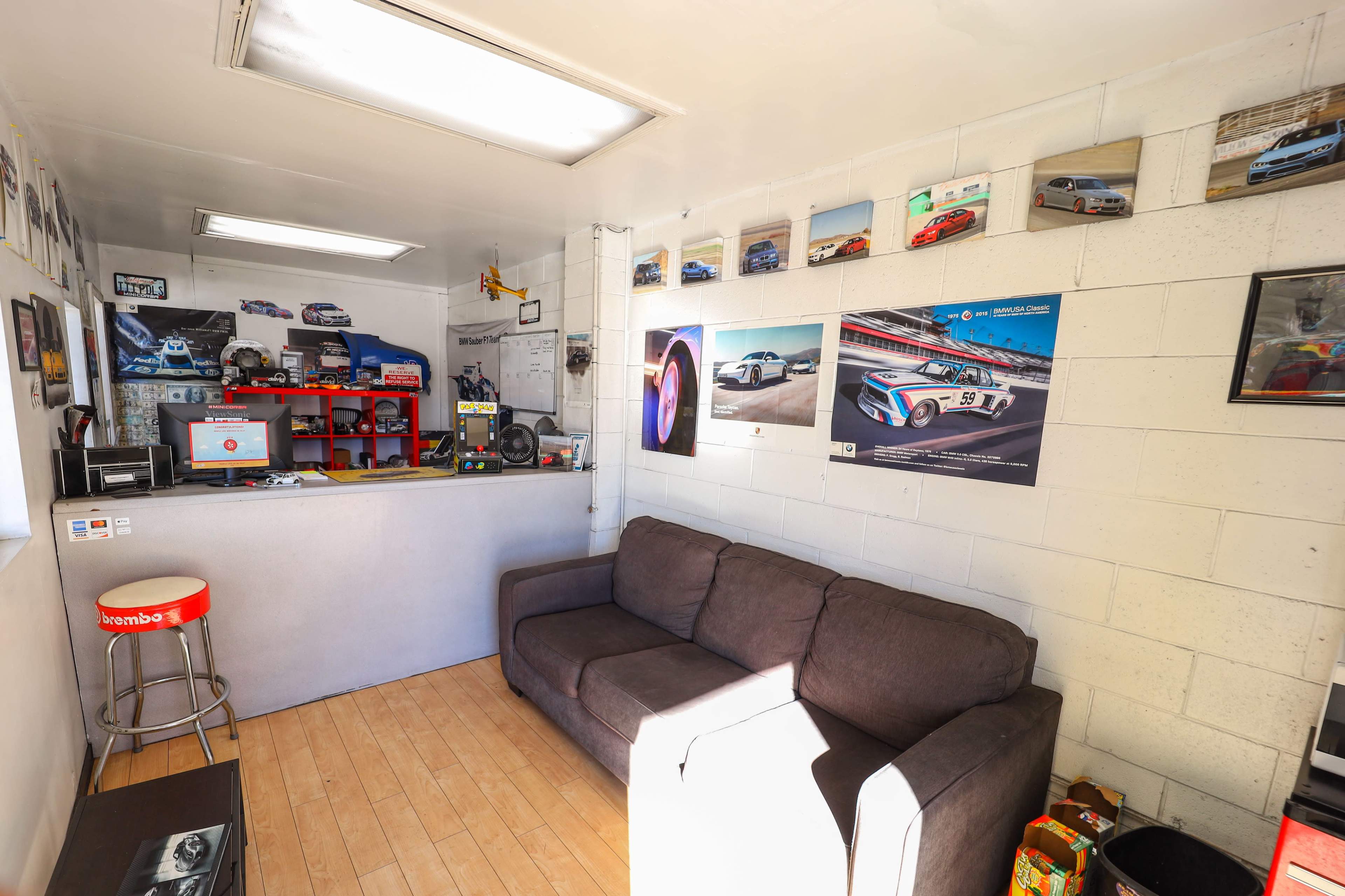 A small office space featuring a gray couch, a reception counter with a computer, and walls adorned with car-themed posters and photographs.
