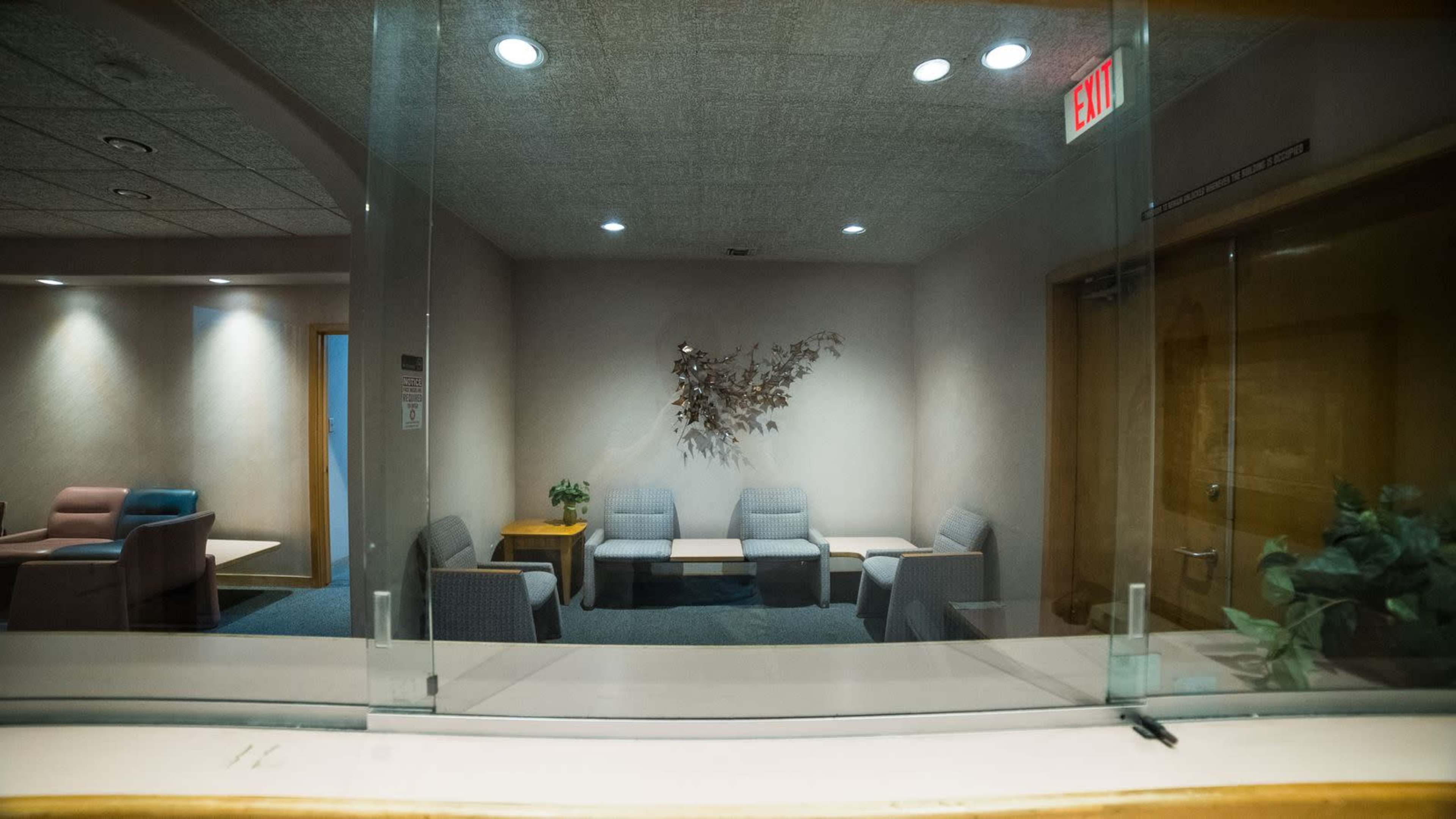 The image shows a waiting area with several chairs arranged around a small table, visible through a glass partition.