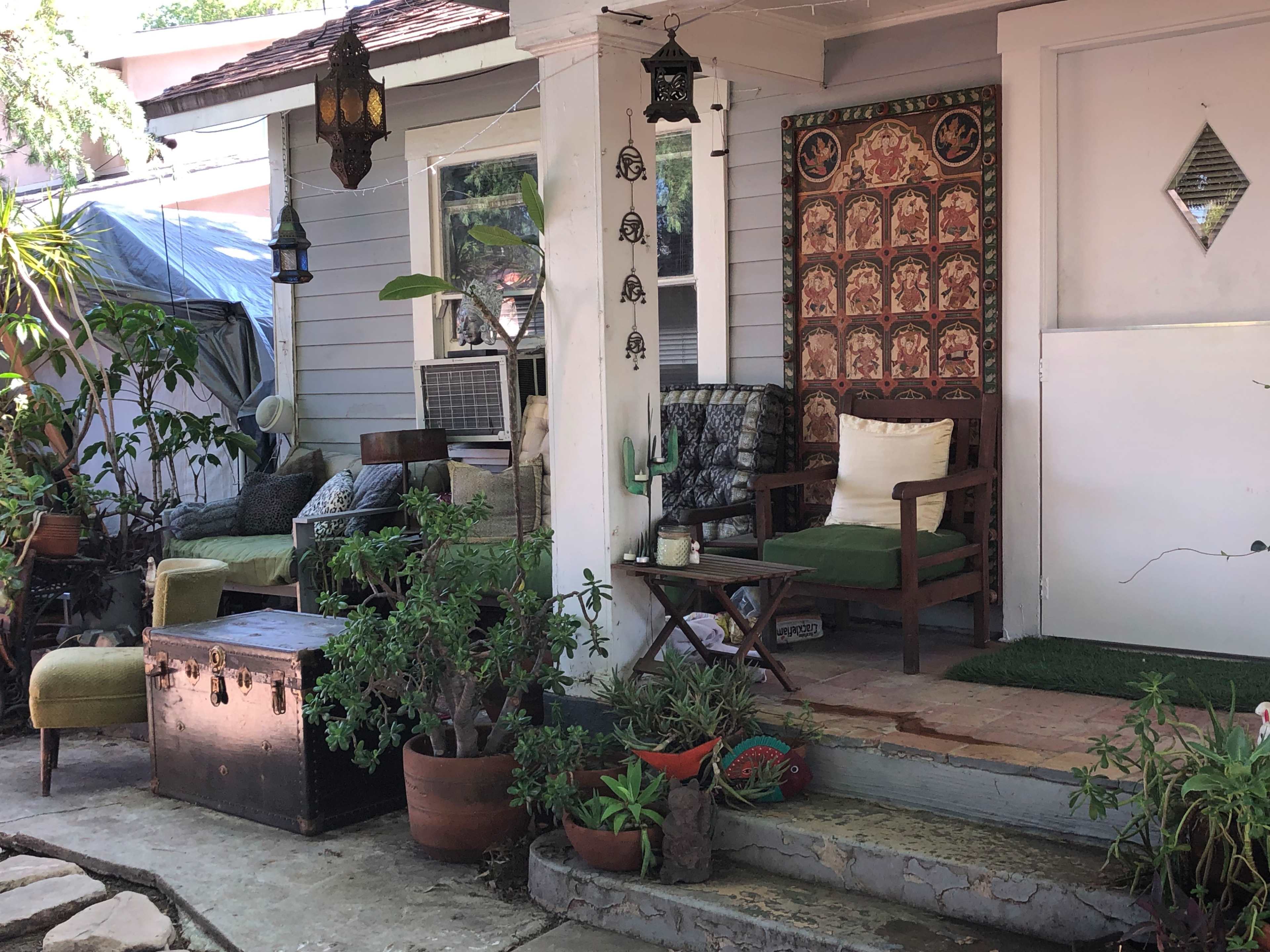 A porch with a variety of seating, potted plants, and decorative items, including a lantern and a patterned wall hanging.