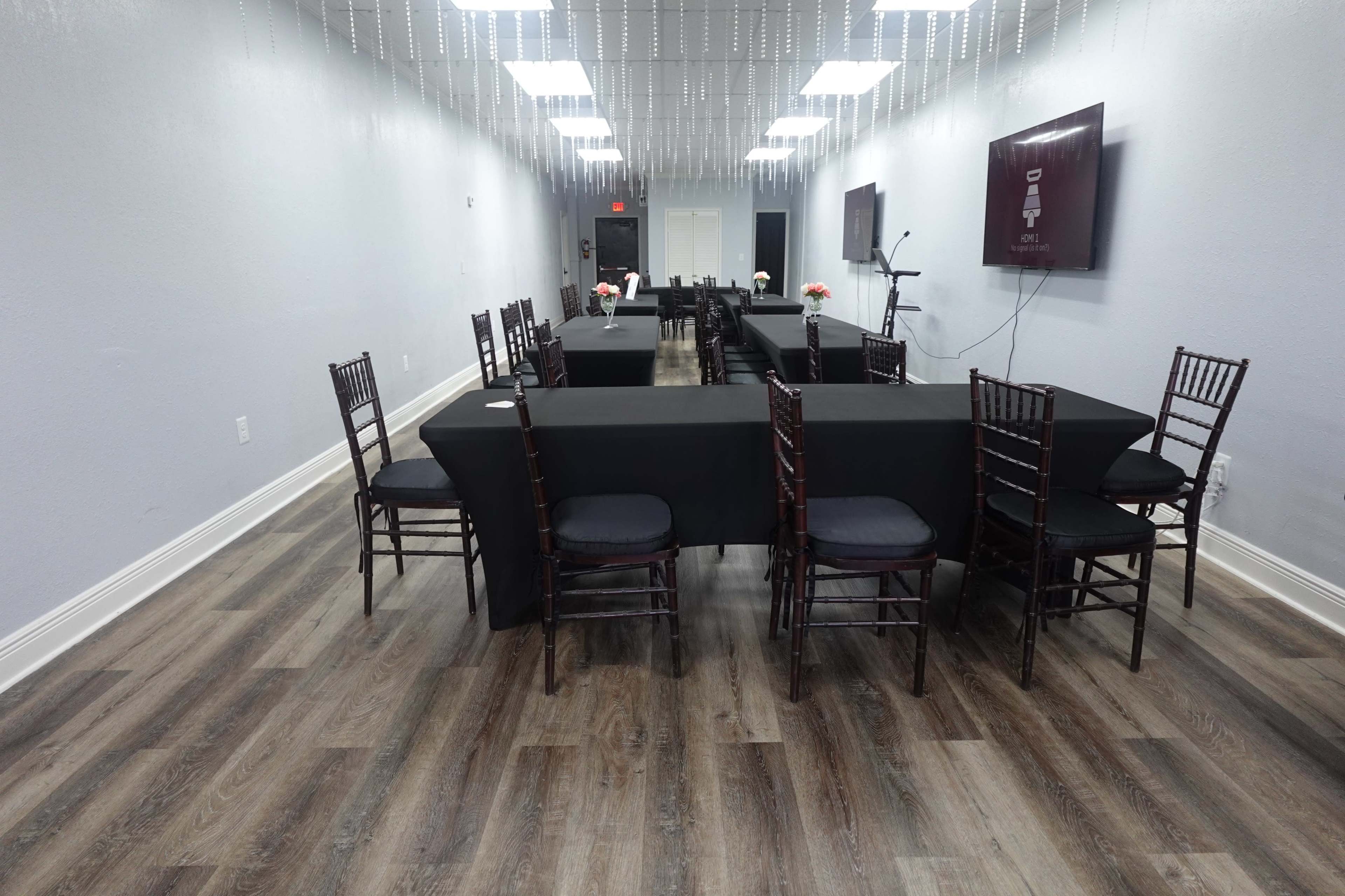 The interior of a spacious room features several rectangular tables covered with black tablecloths and surrounded by dark wooden chairs.