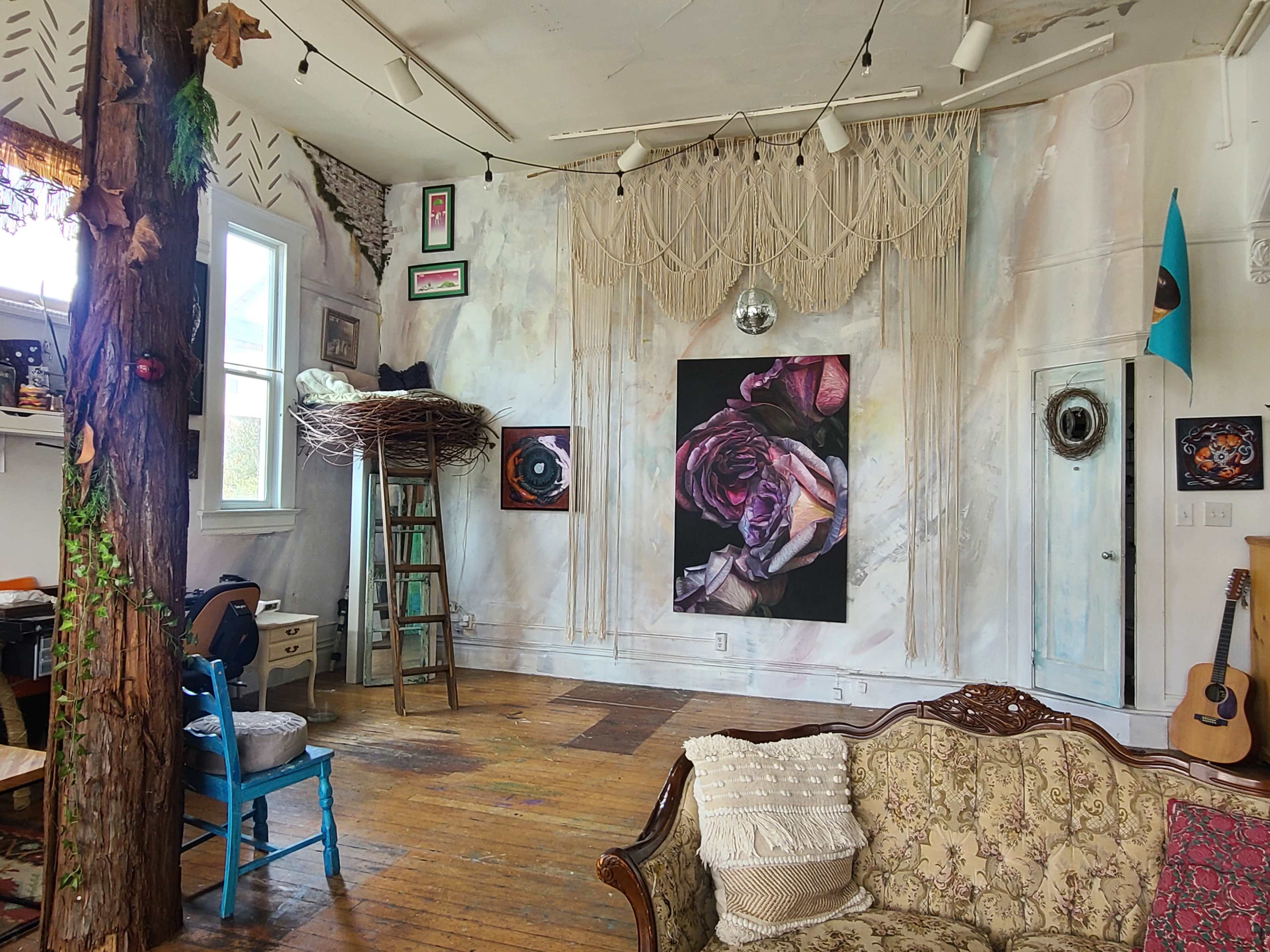 A creative interior space with a floral painting on the wall, a wooden ladder leading to a lofted area, and a vintage-style couch in the foreground.