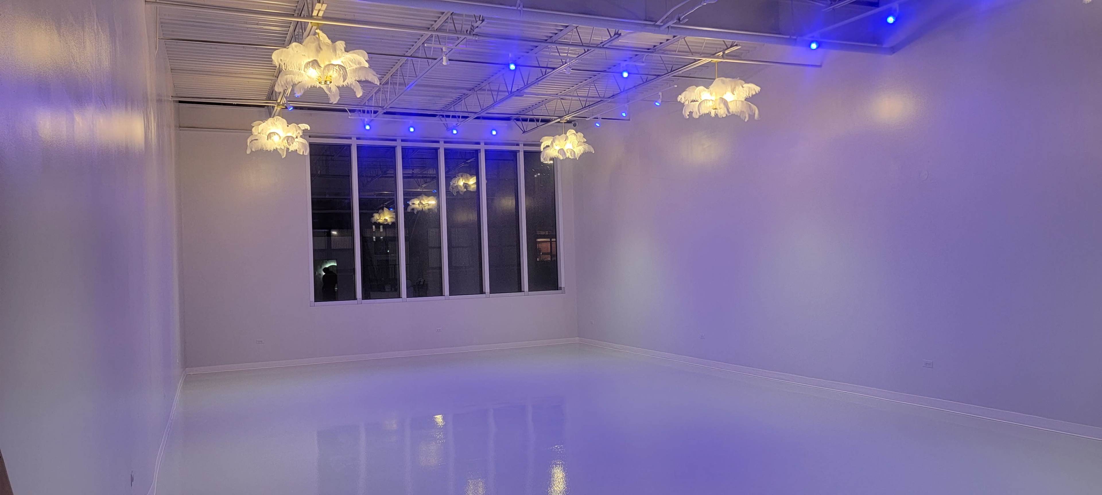 The image shows a spacious, well-lit room with polished white floors and several pendant lights hanging from the ceiling.