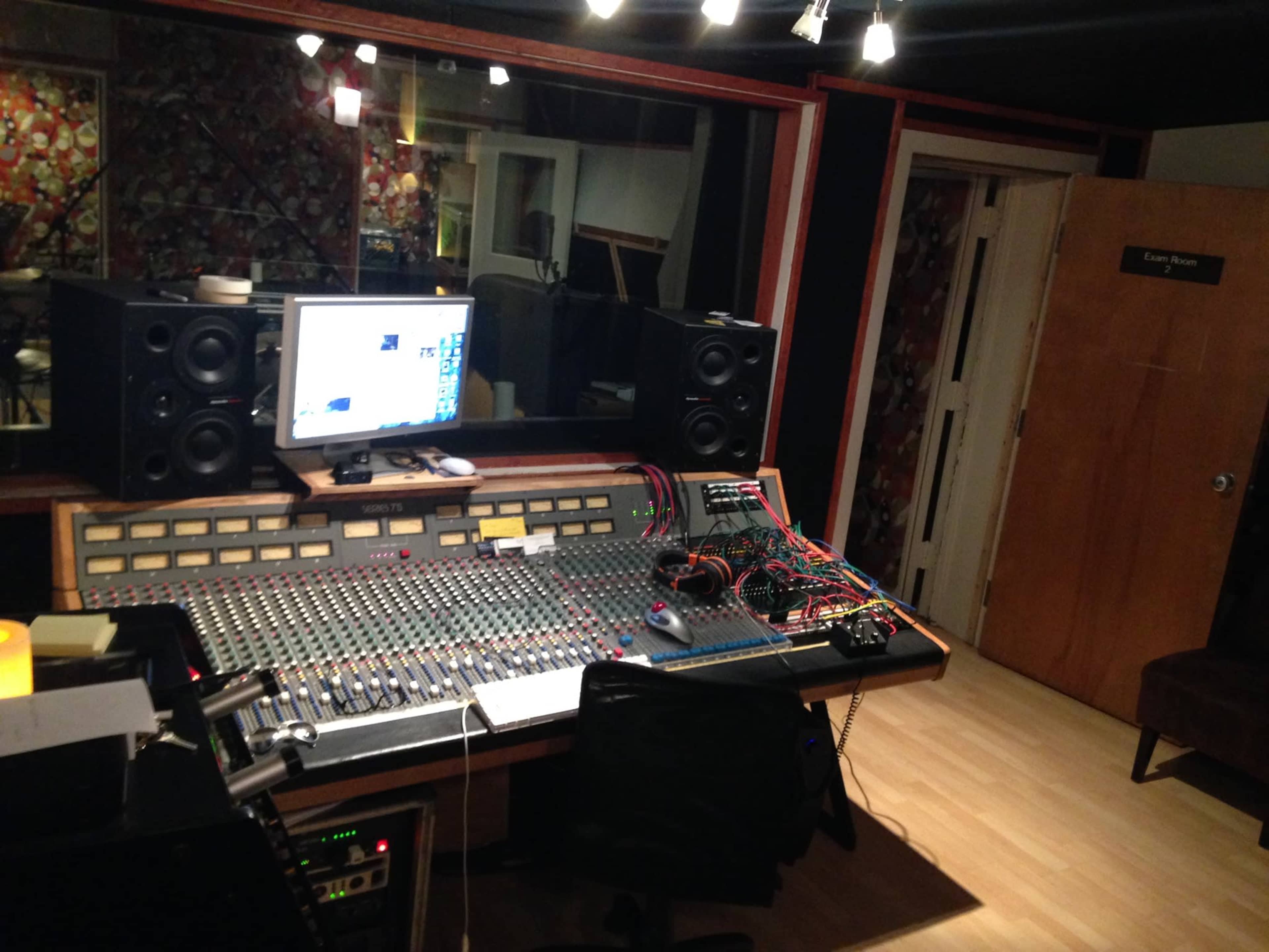 A recording studio with a large mixing console, computer monitor, and various audio equipment, surrounded by soundproofing materials.