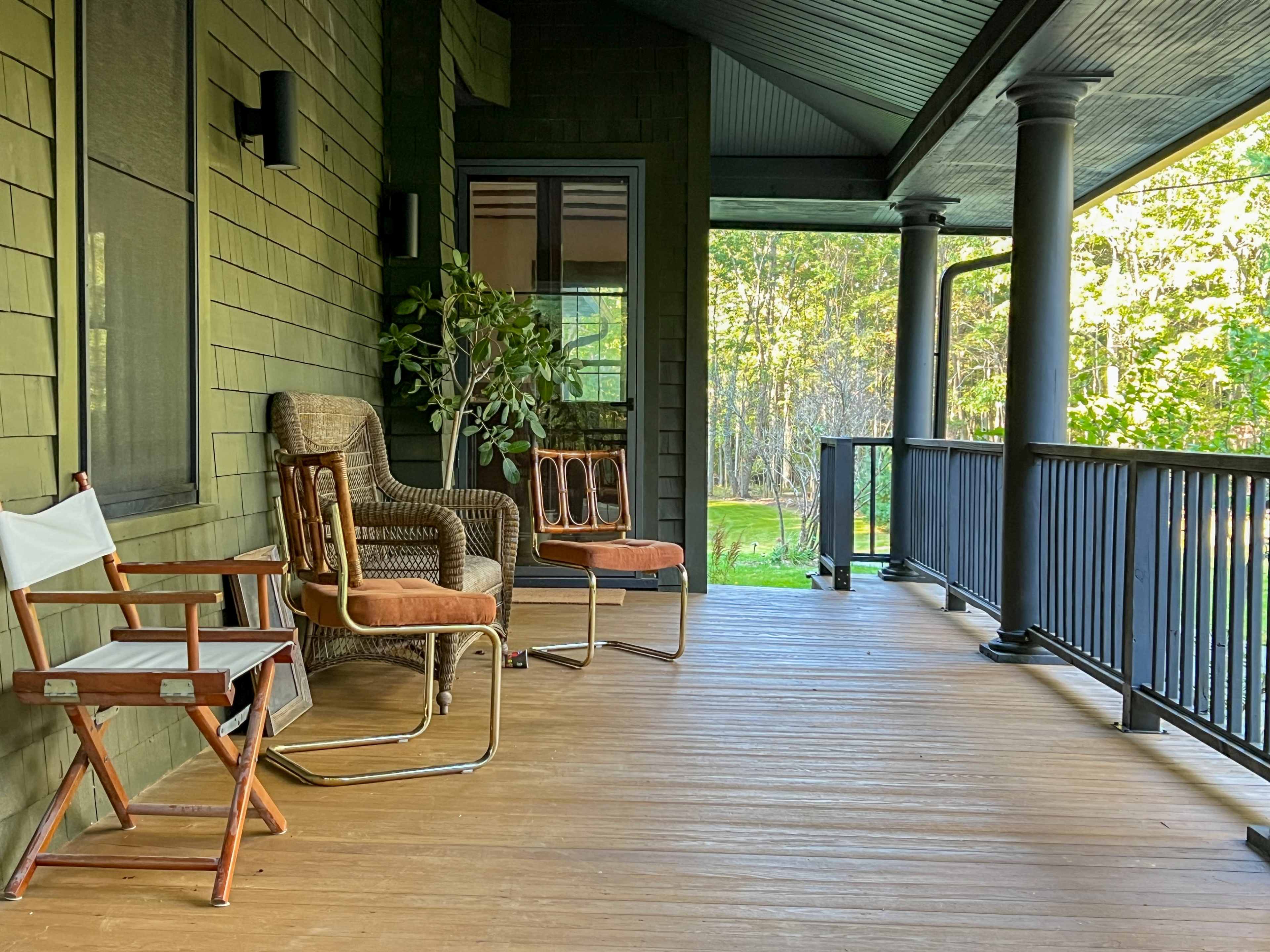 The image shows a spacious porch with three wooden chairs and a potted plant, surrounded by green trees.