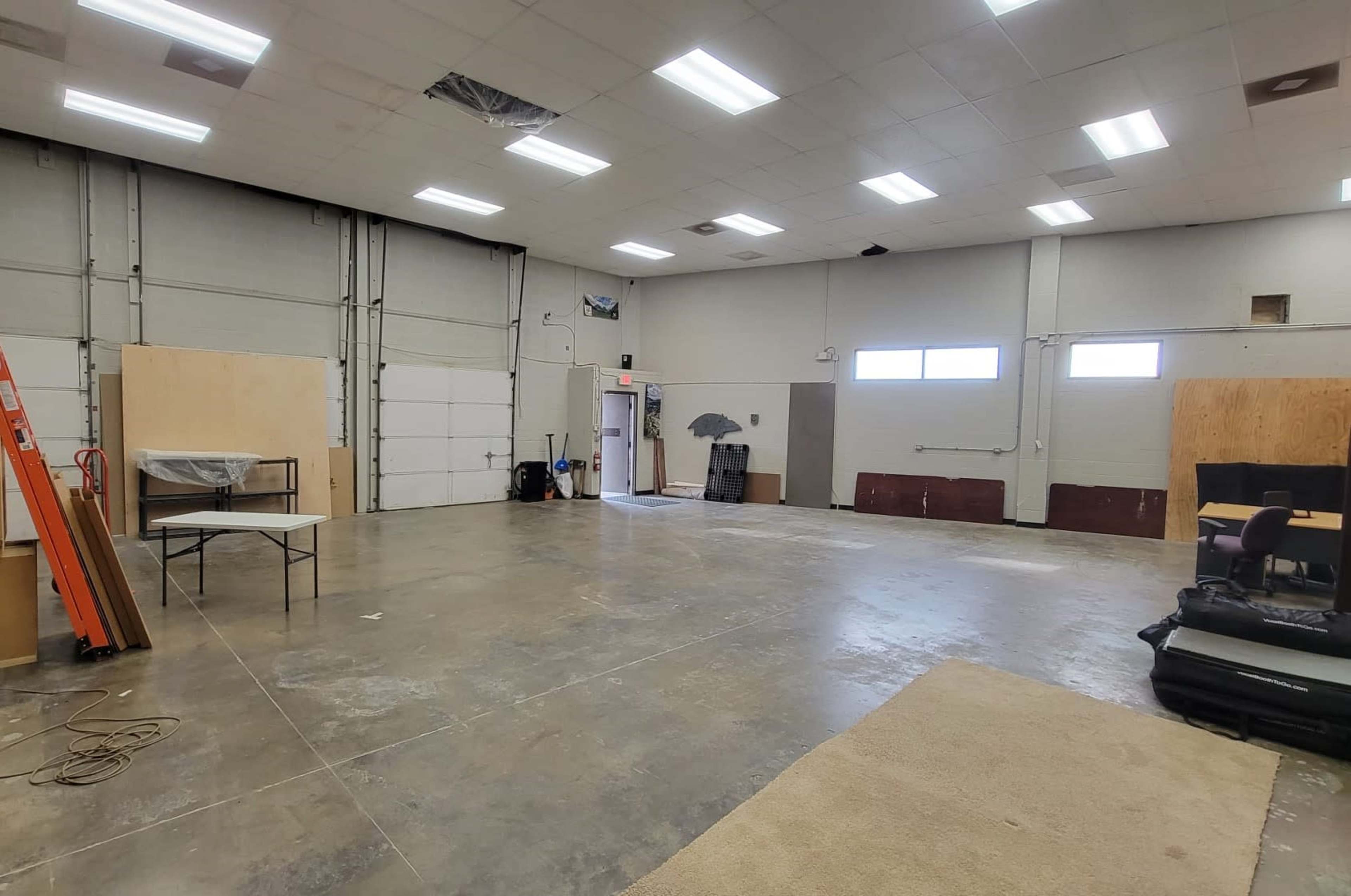 A spacious, empty warehouse interior with concrete floors, a few wooden partitions, and an entrance door in the background.