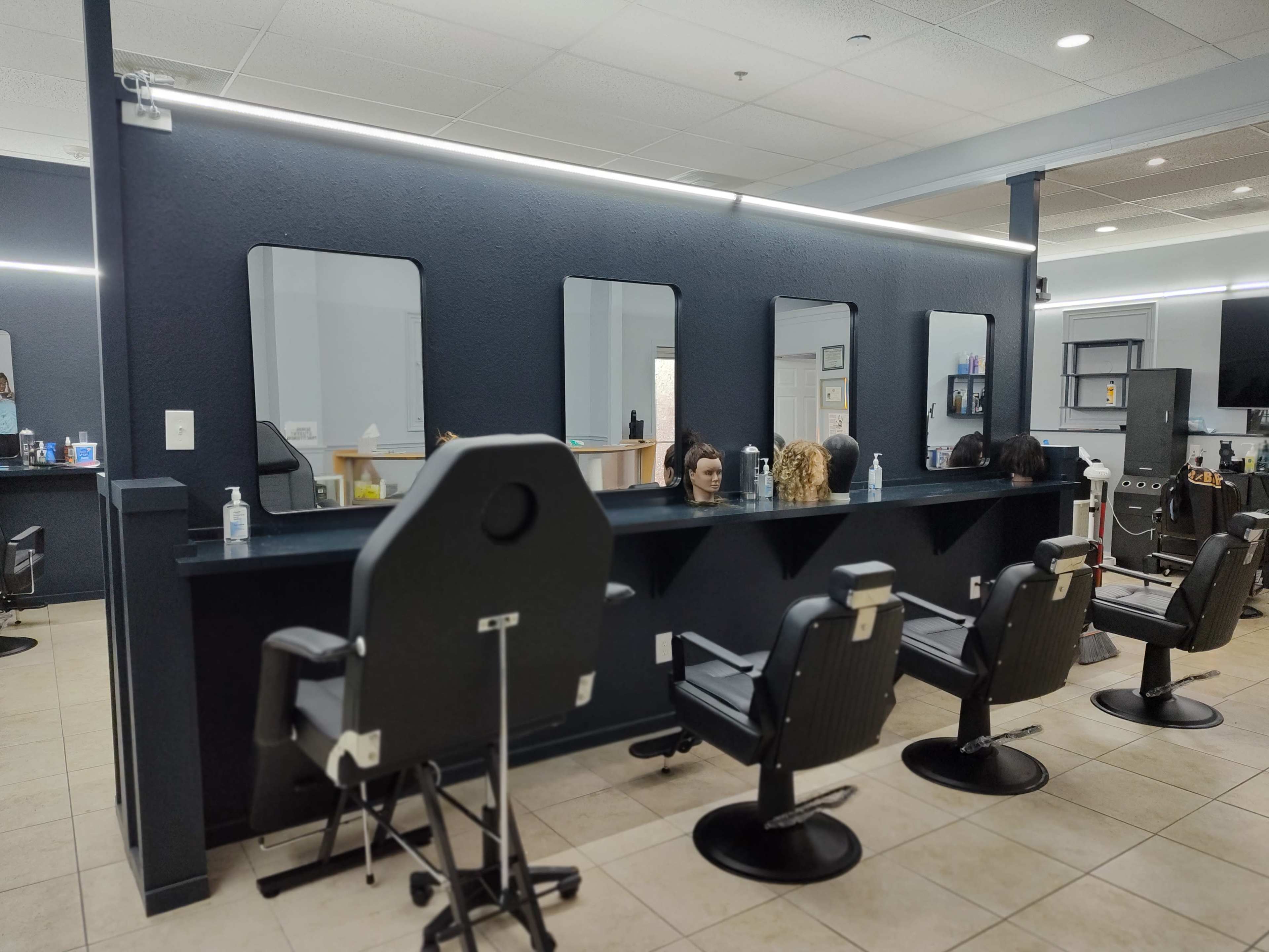 A hair salon with four barber chairs positioned in front of three mirrors, illuminated by LED lights, against a dark wall.