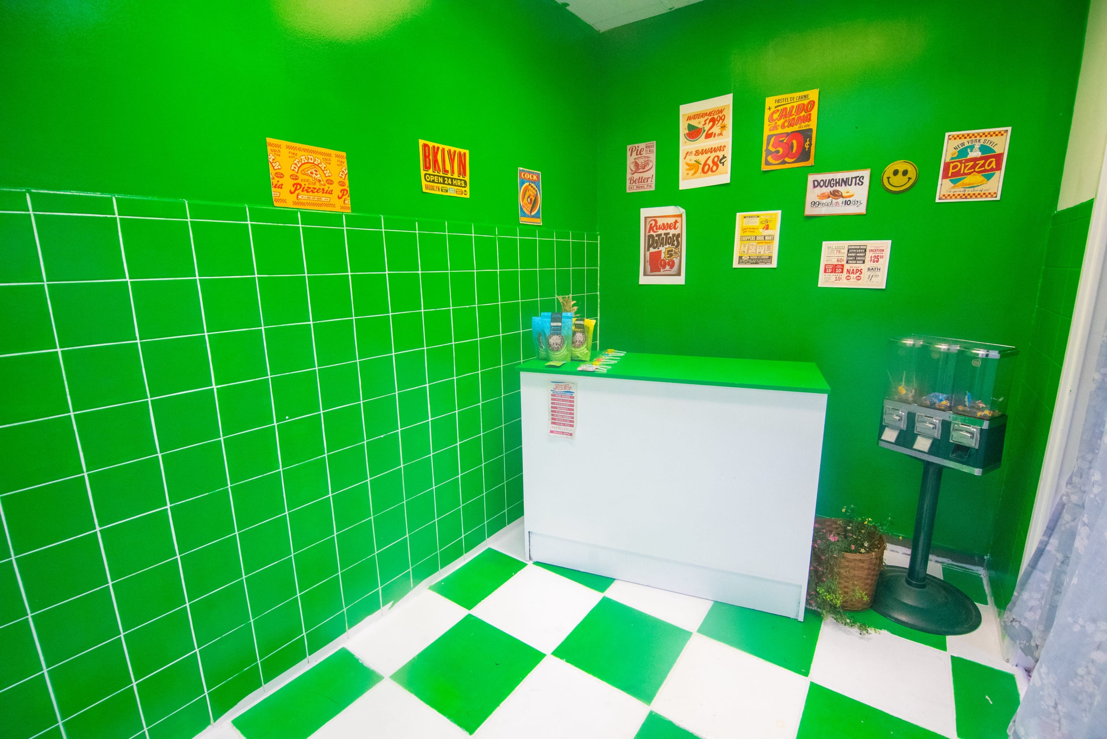 A small room with green walls and a green and white checkered floor, featuring a counter with various colorful signs on the walls.