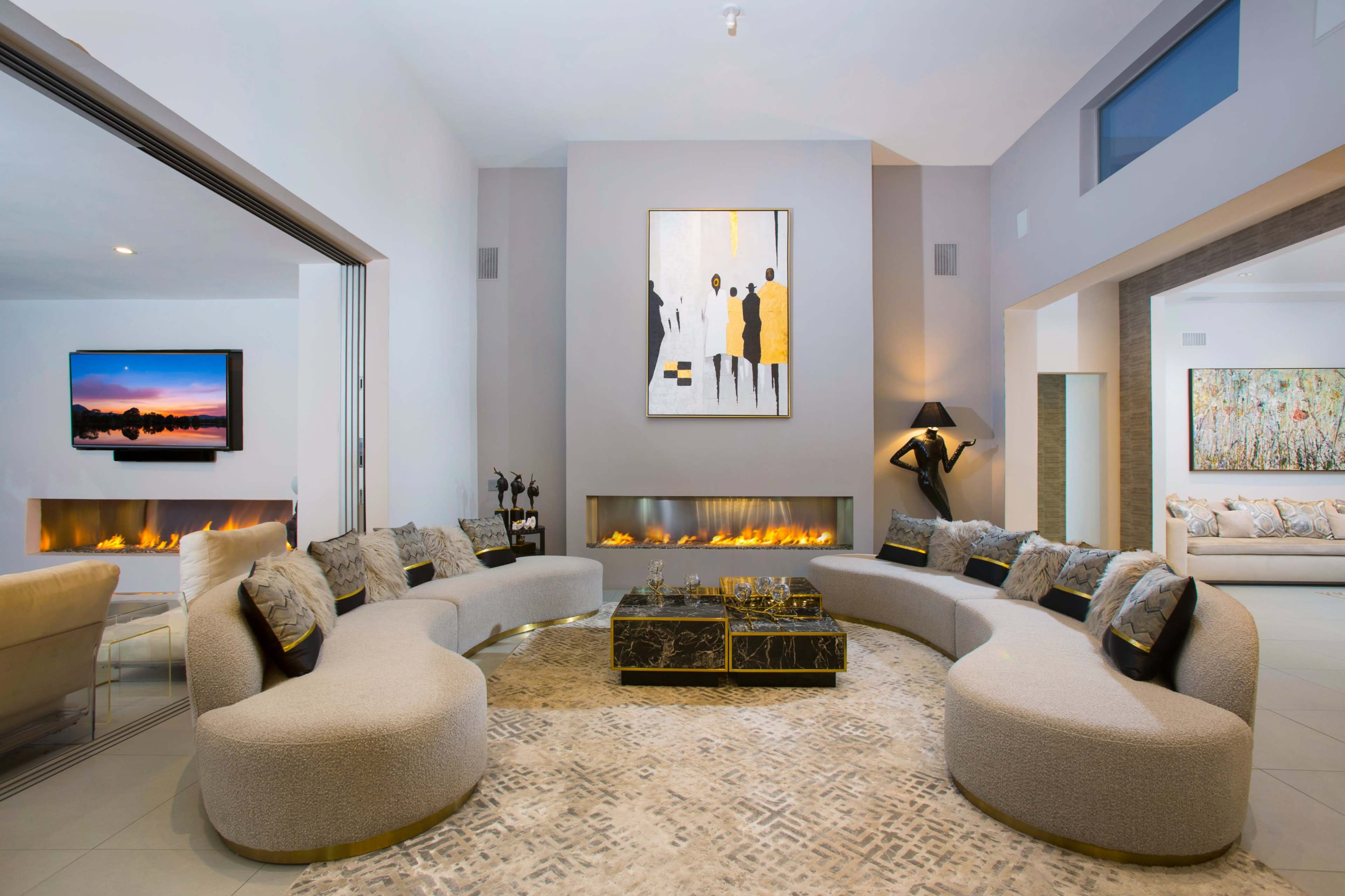 A modern living room features a curved seating area, a large abstract painting, and a long, linear fireplace.