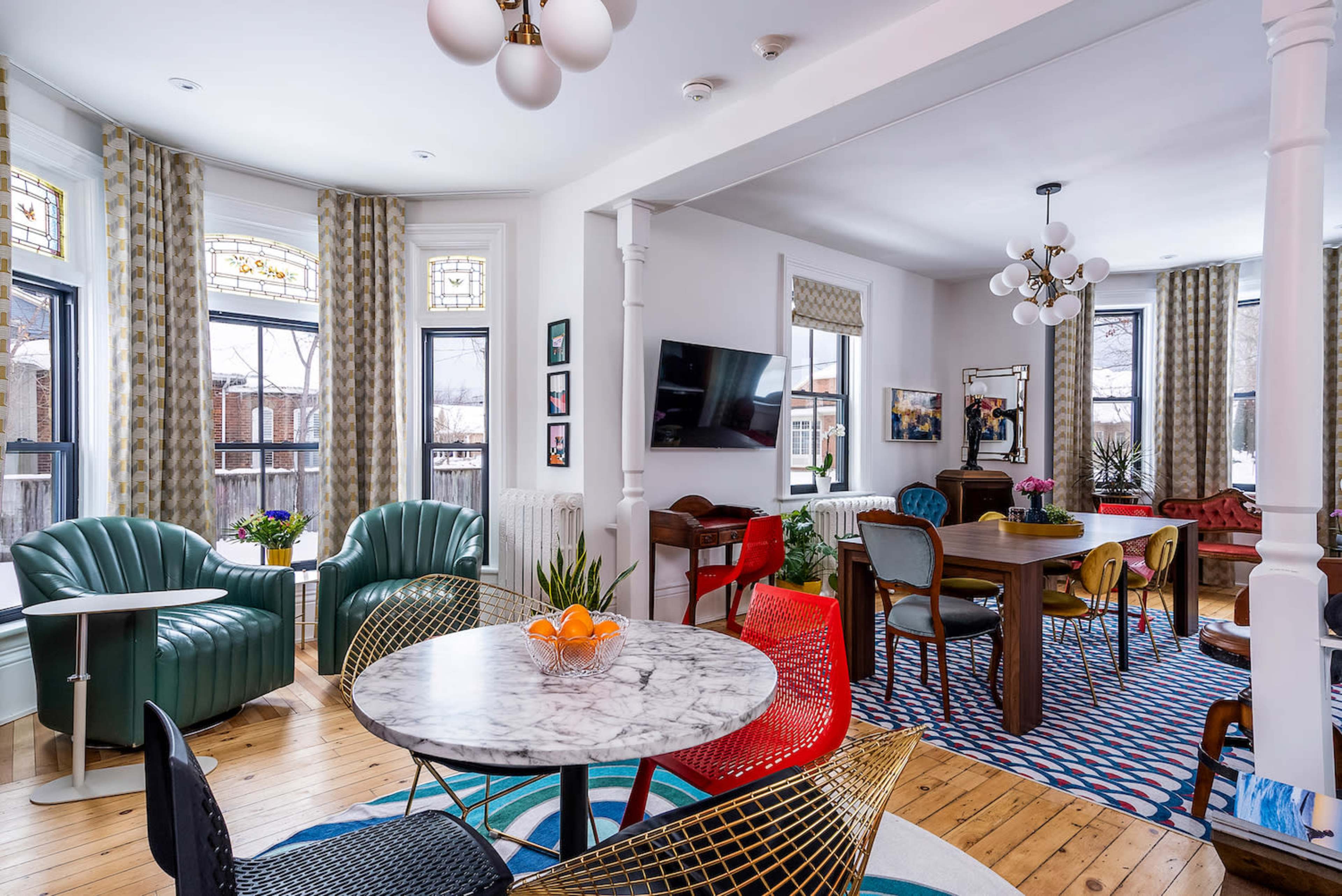 A modern, open-concept living and dining area featuring a marble table, colorful chairs, and large windows with patterned curtains.