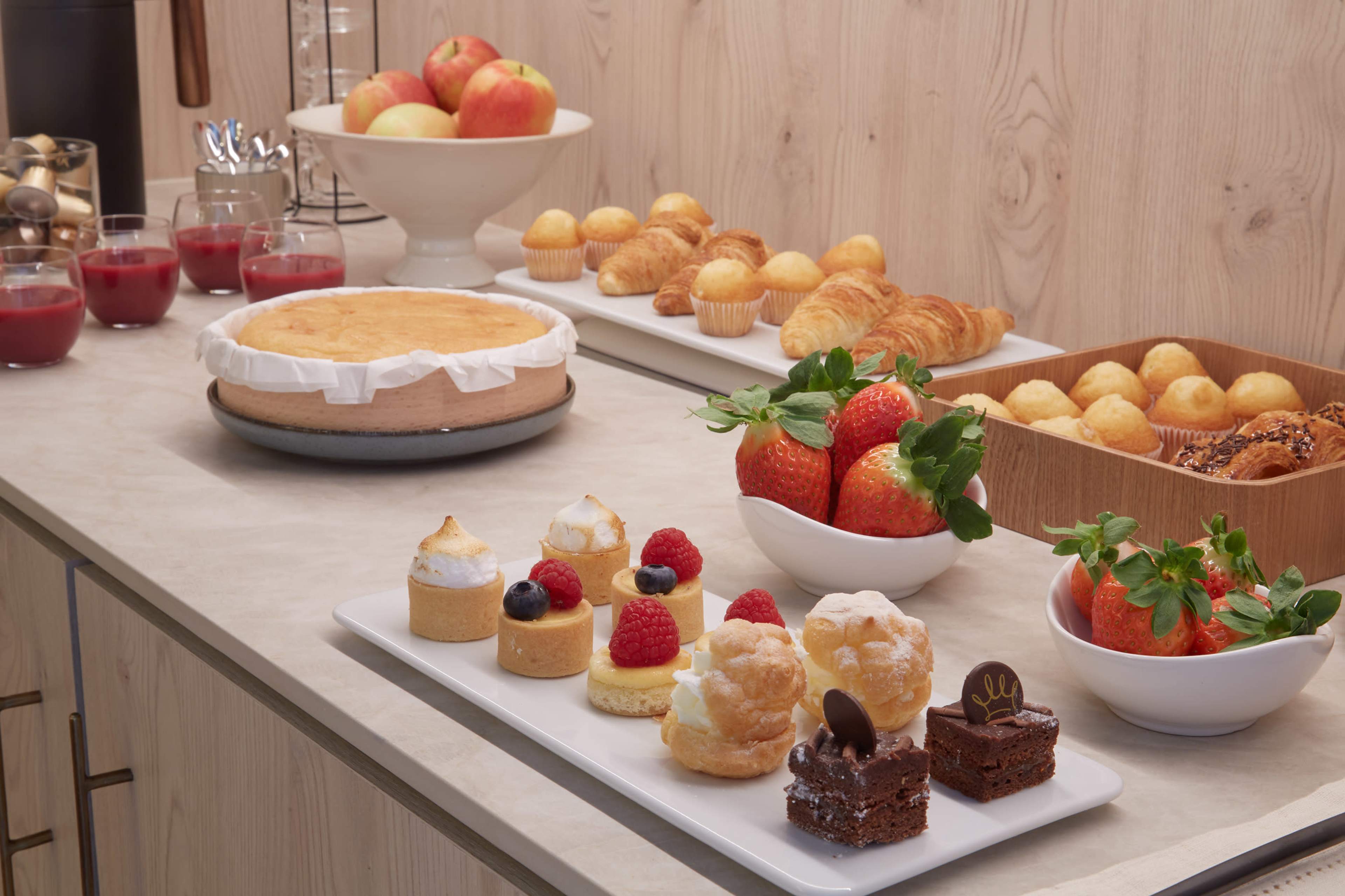 A variety of desserts and pastries, including cakes, fruit, and pastries, are displayed on a countertop.