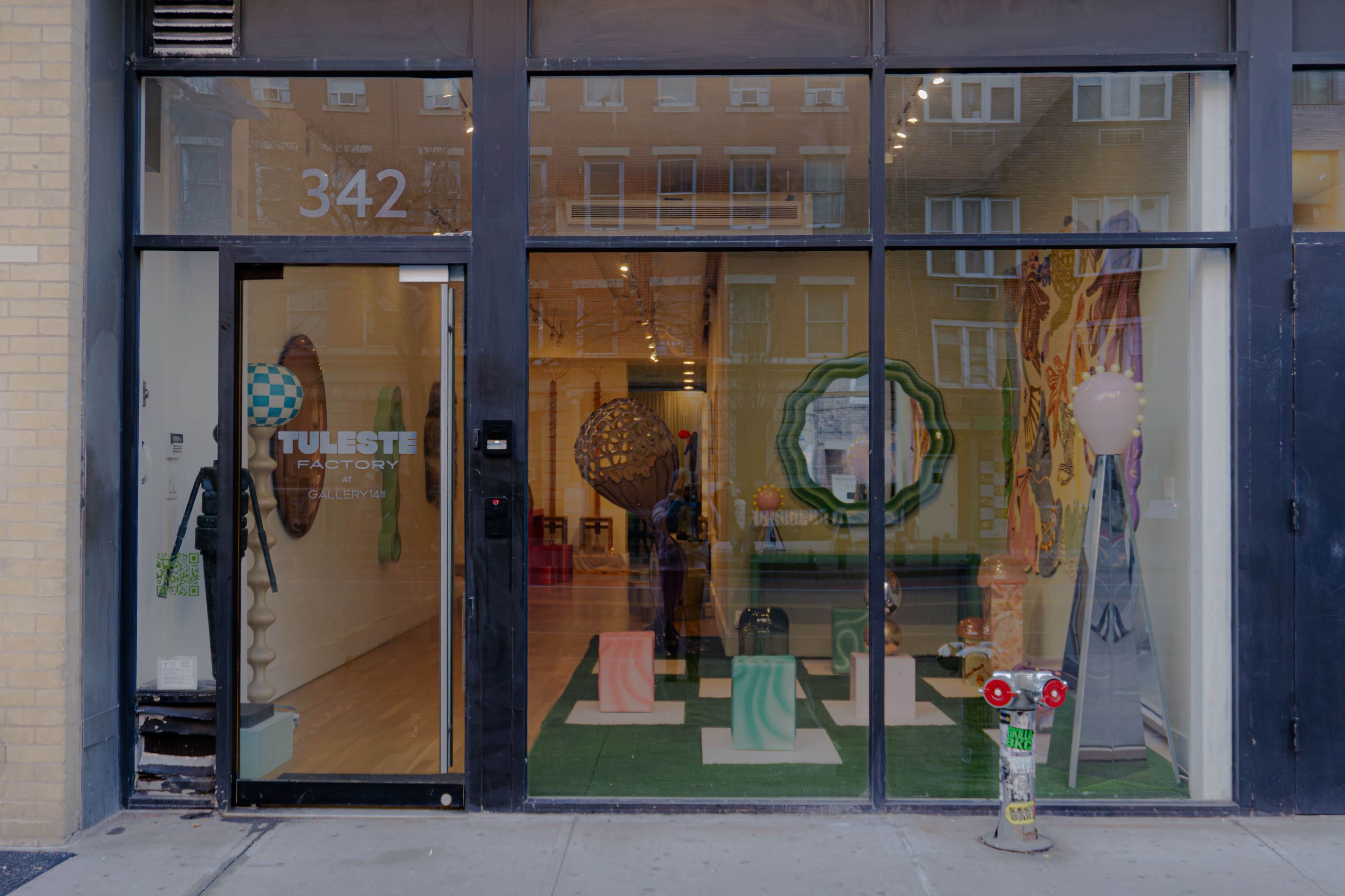 The storefront of Tuleste Factory features large glass windows displaying colorful sculptures and art inside the gallery.