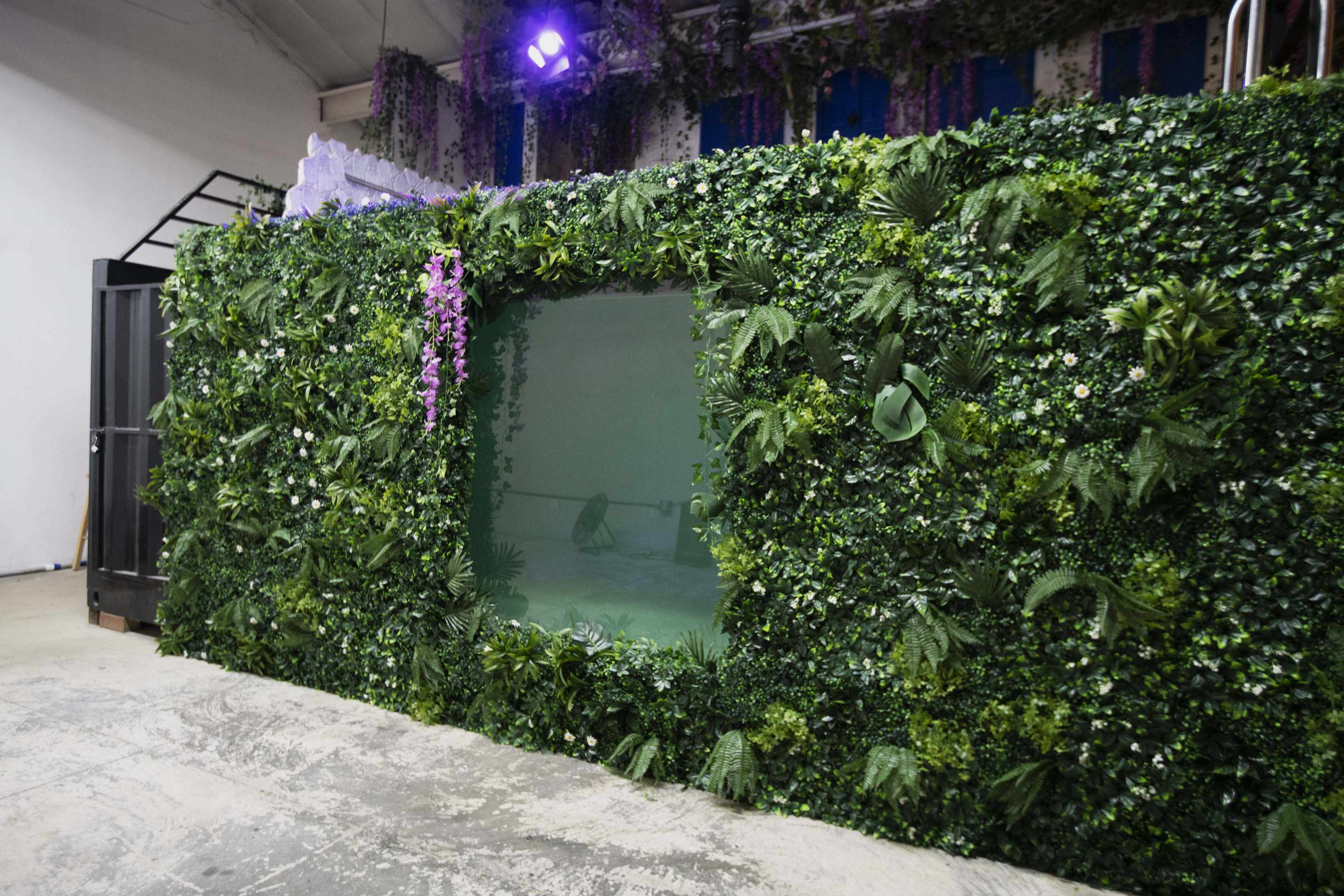 A wall covered in greenery, featuring a large rectangular opening, stands in a spacious room with industrial elements.