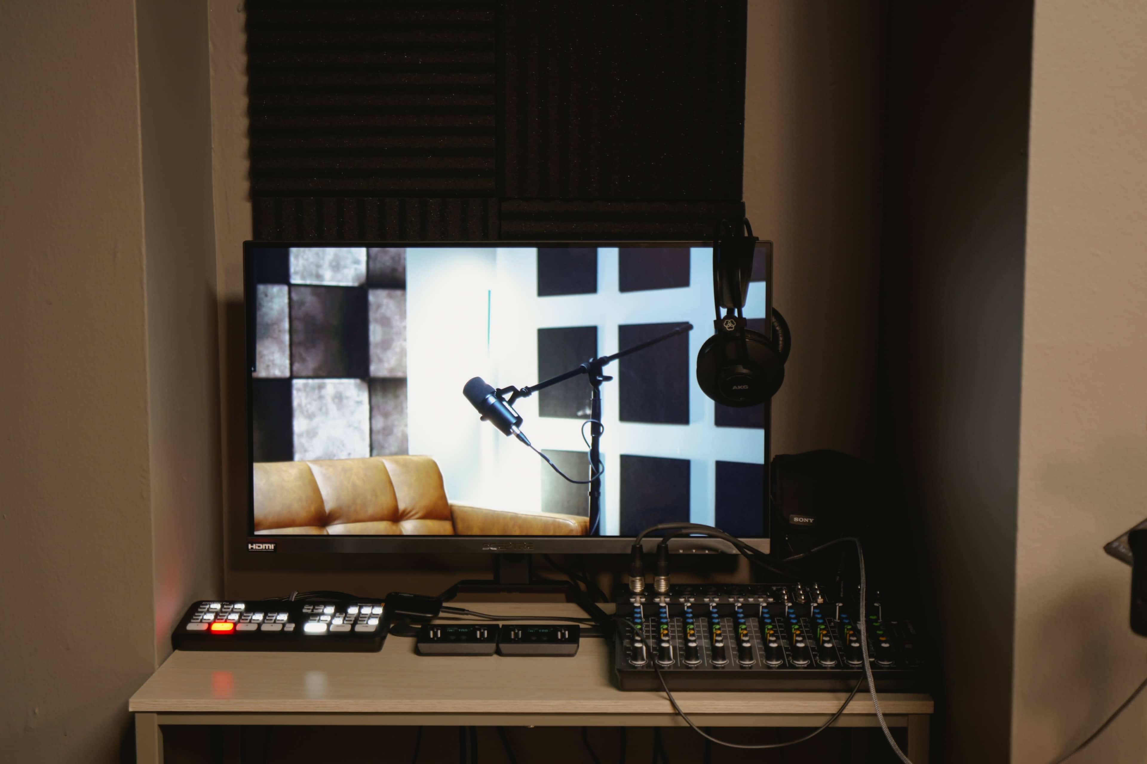 The image shows a computer monitor displaying a microphone setup, with a brown couch and a sound mixing console on a desk.
